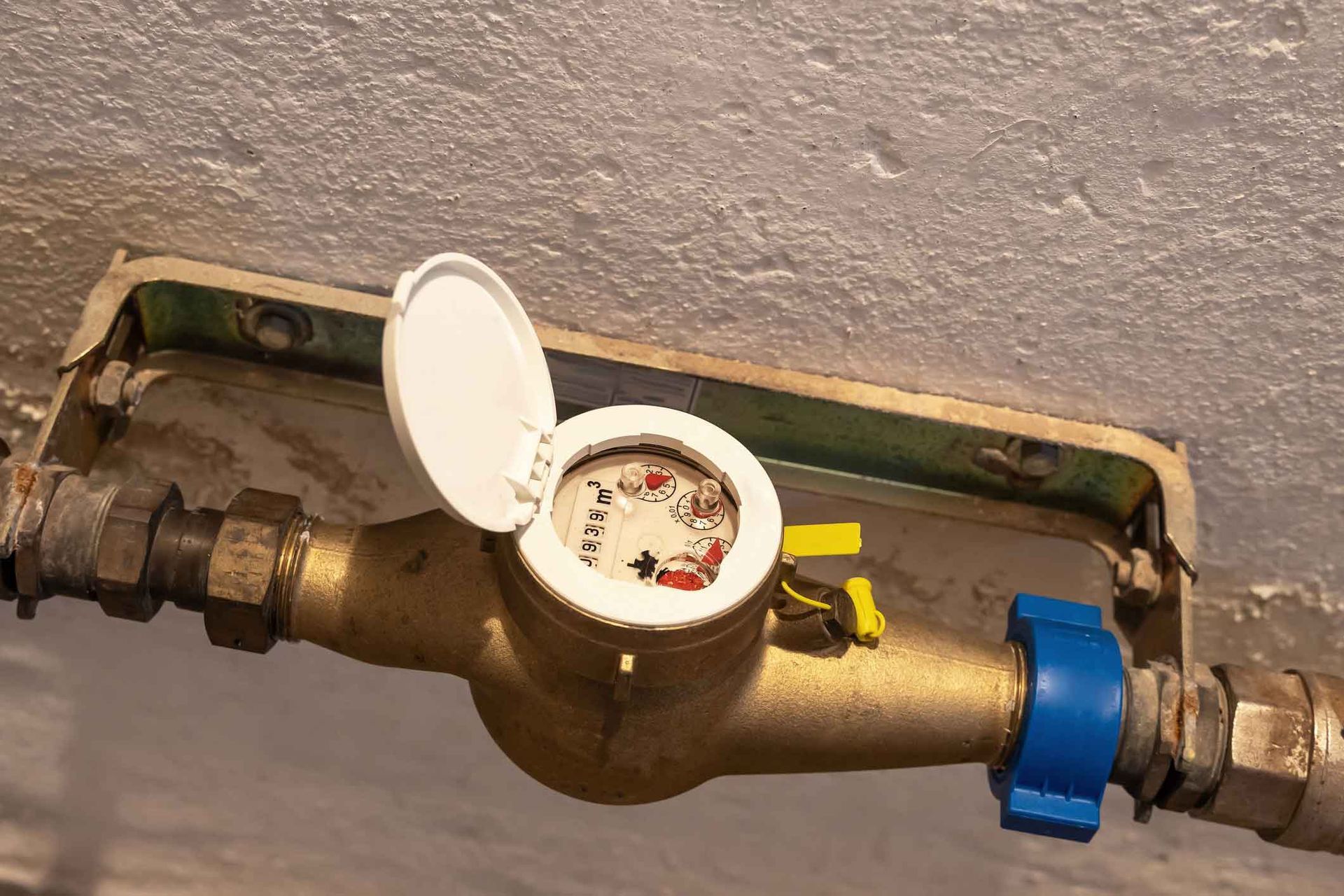 A water meter is attached to a pipe on a wall.