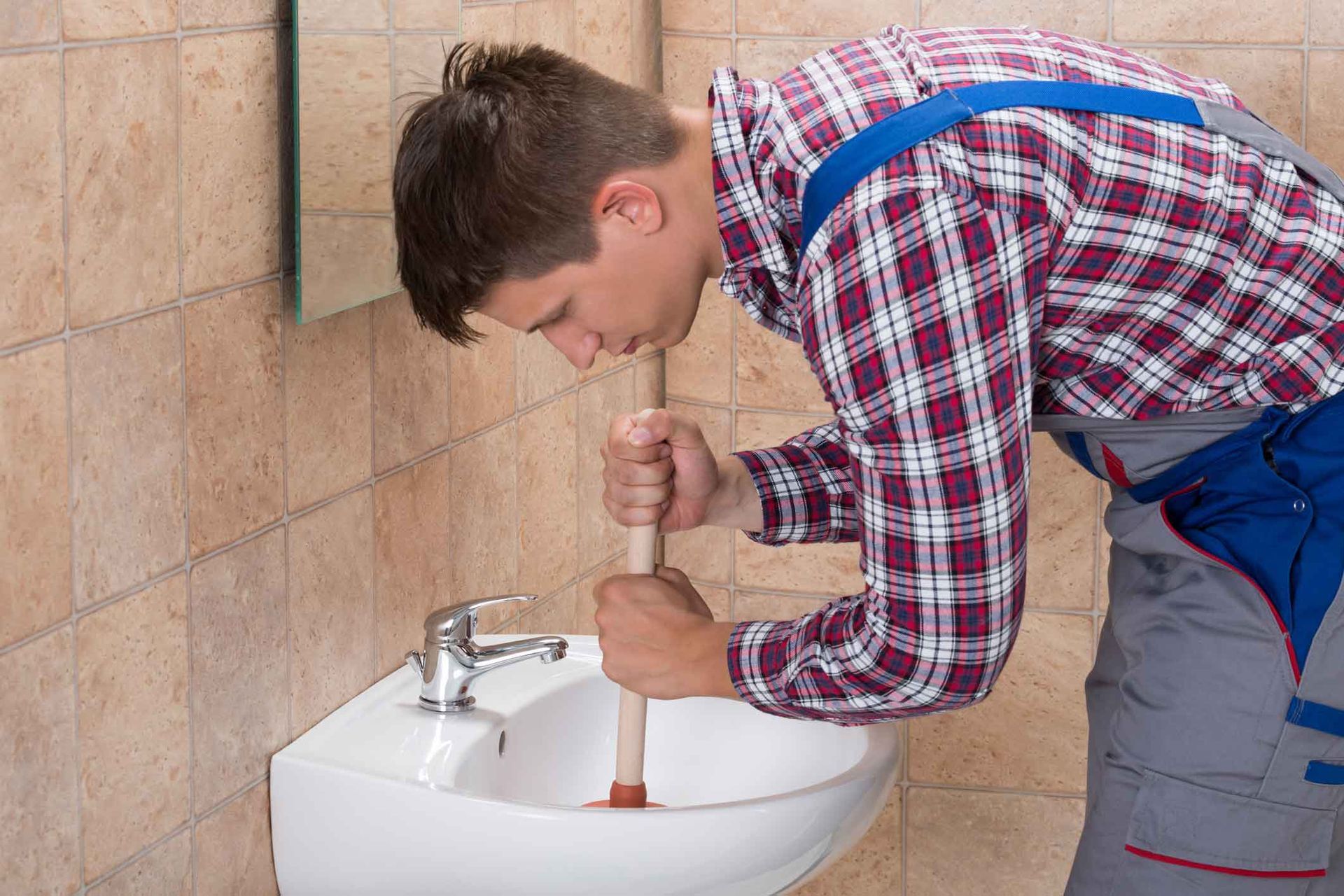 A man is using a plunger to unblock a bathroom sink.