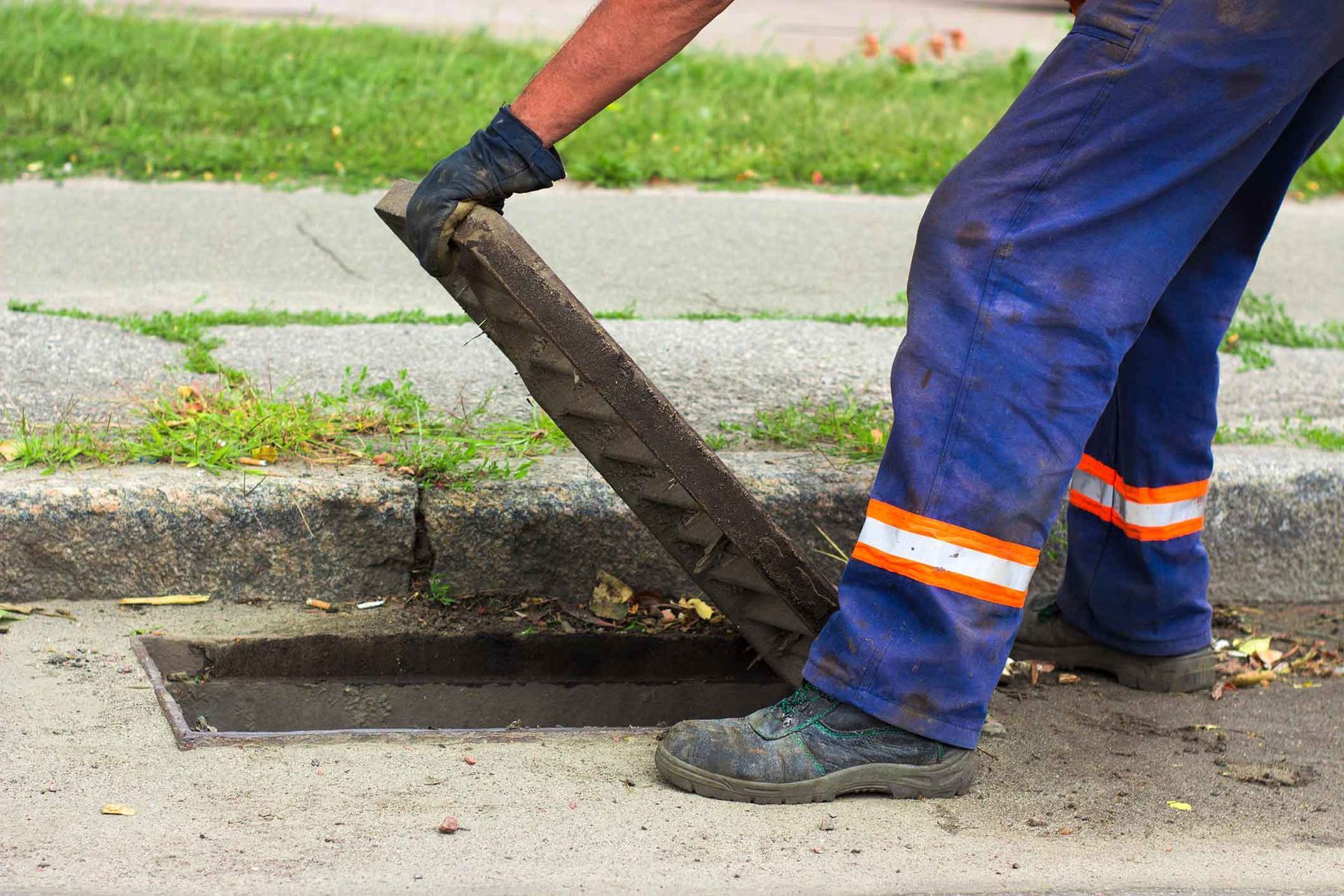 A man is opening a manhole cover on the side of the road.