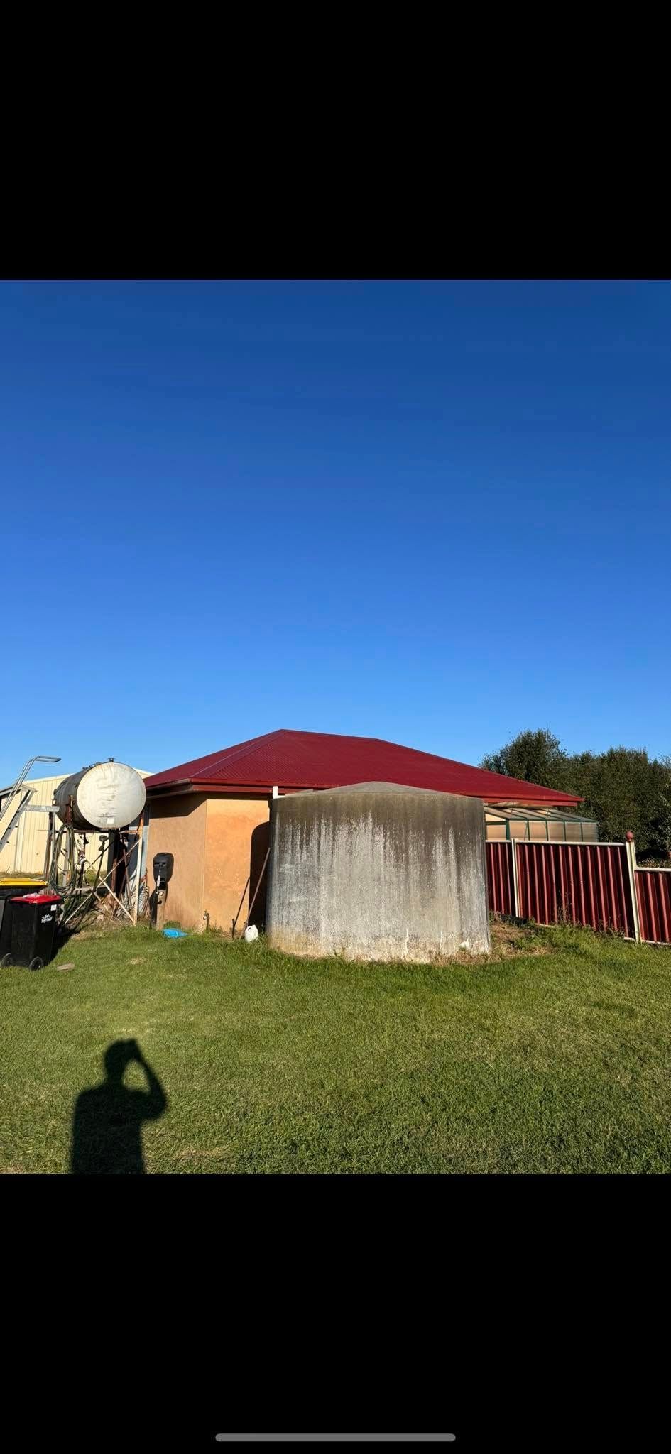 A house with a red roof is sitting in the middle of a grassy field.