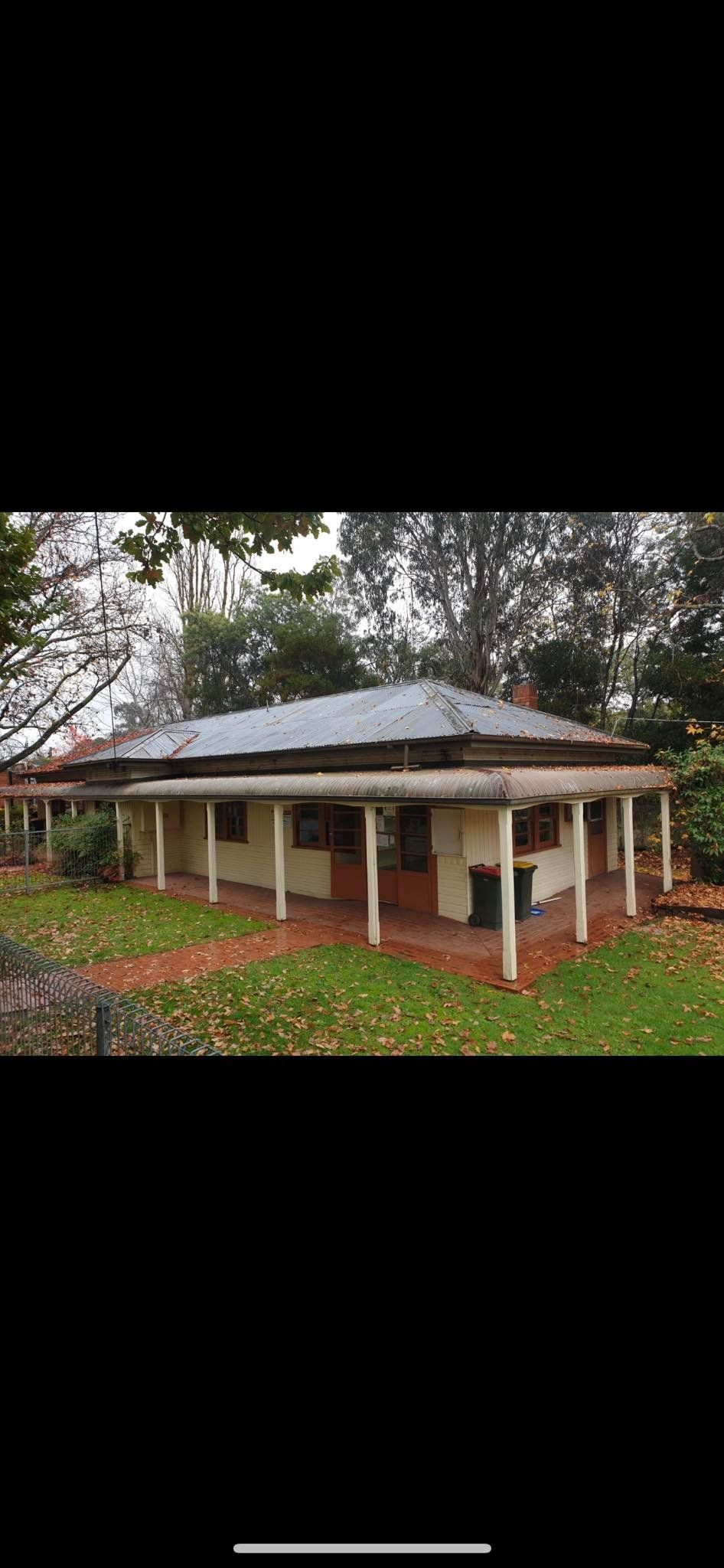 A house with a porch and a metal roof is sitting on top of a lush green field.