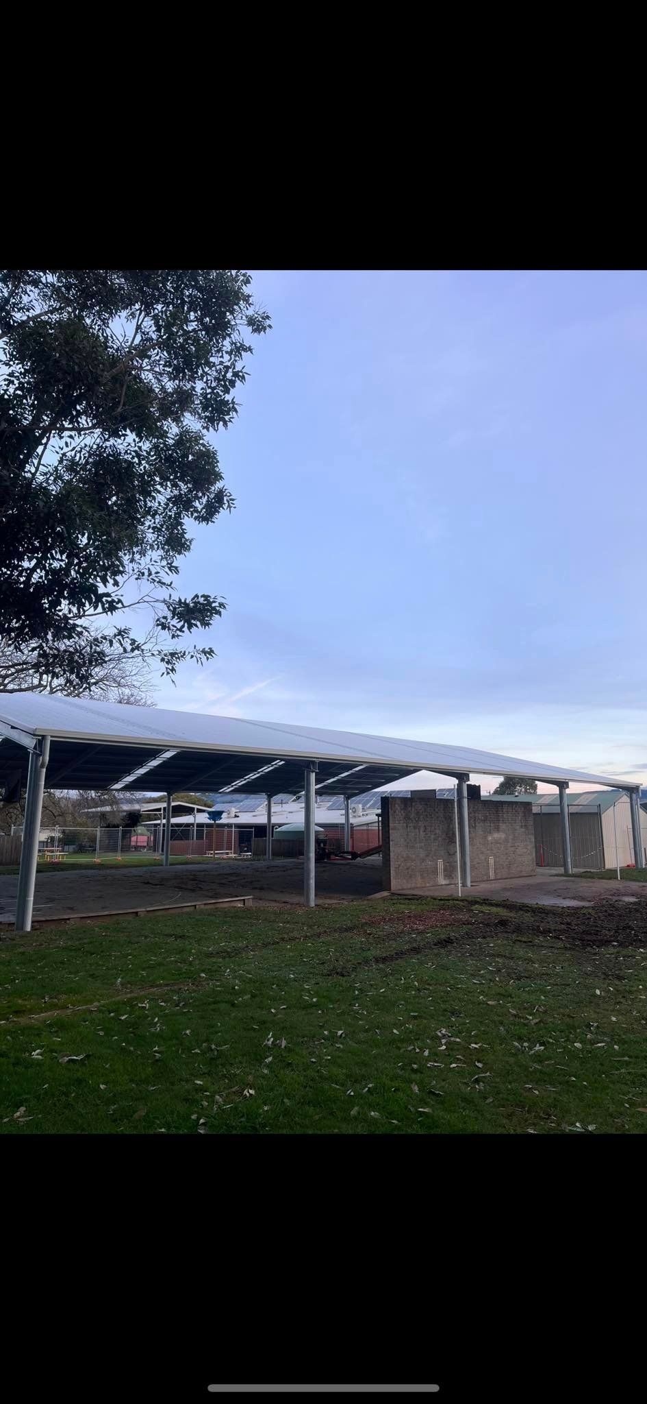A carport with a tree in the foreground and a blue sky in the background.