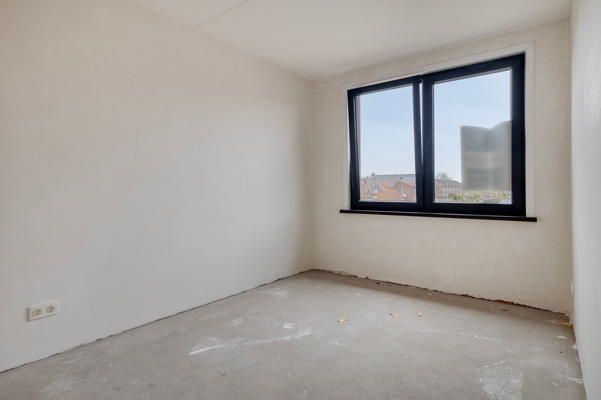 Lege kamer met raam, witte muren en een lichtgekleurde vloer.