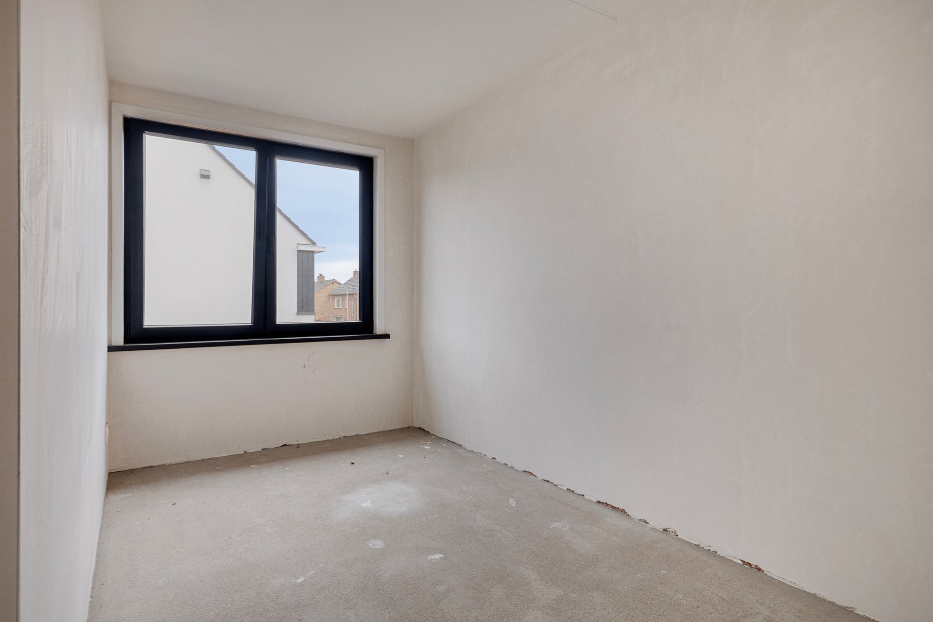 Lege kamer met onafgewerkte muren, raam en betonnen vloer.