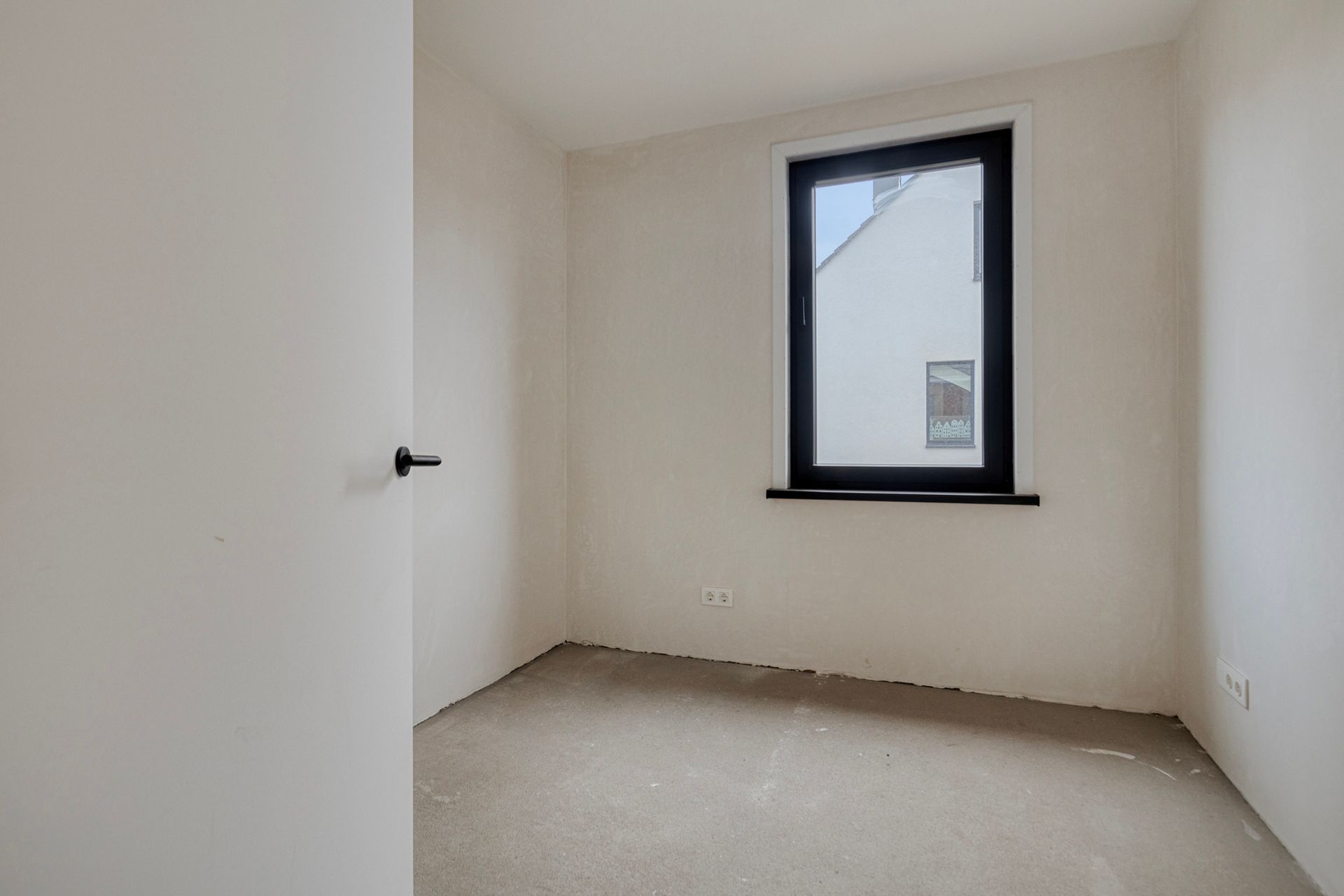 Een lege kamer met onafgewerkte muren, een raam en een deur.