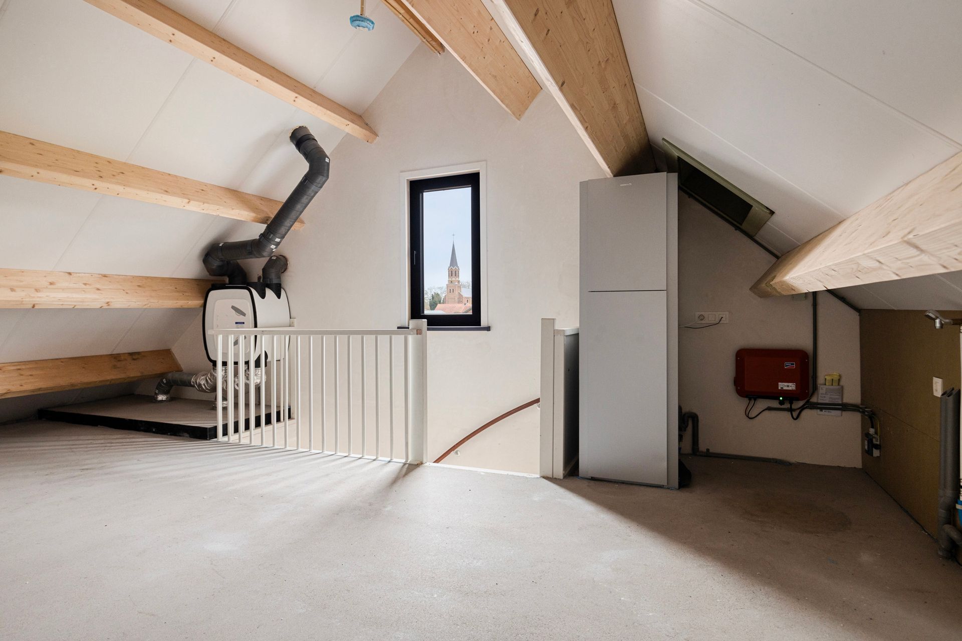 Zolderinterieur met zichtbare balken, een klein raam en apparatuur zoals een verwarmingssysteem en een boiler.