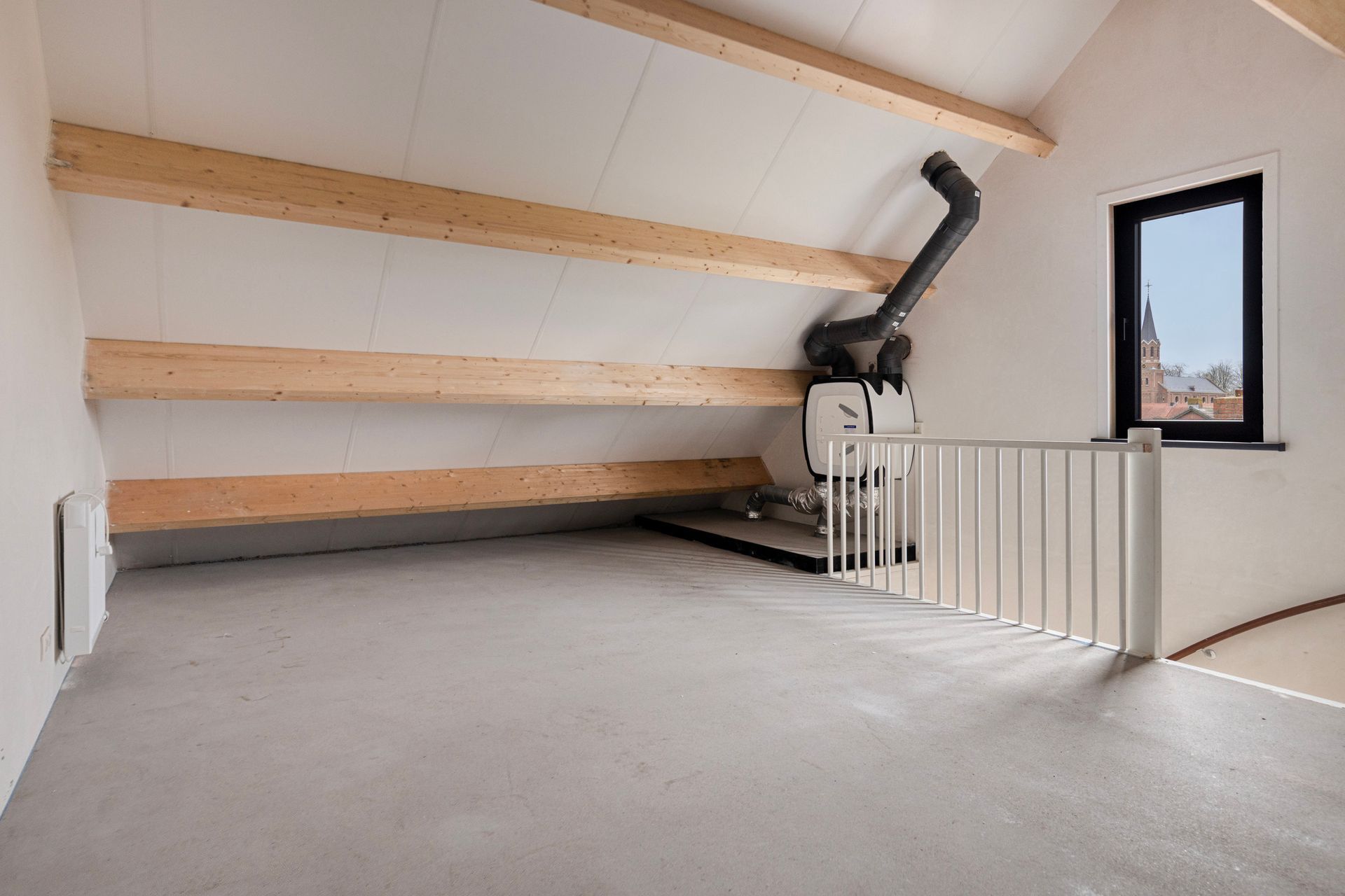 Lege zolderkamer met zichtbare houten balken, een schoorsteen en een raam met een klein traphekje.