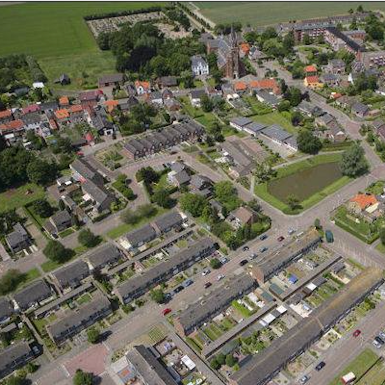 Luchtfoto van een historisch Europees stadje met rode pannendaken, omgeven door groene velden en een gracht.