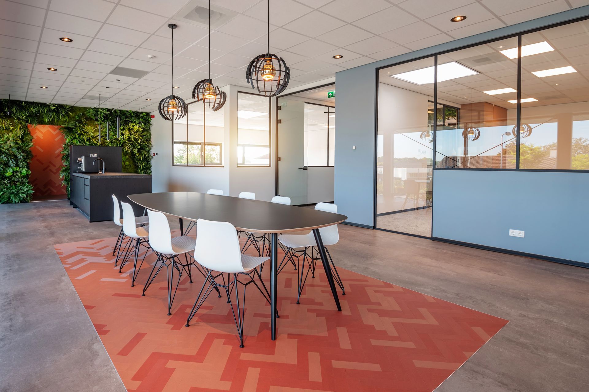 Moderne vergaderruimte met lange tafel, witte stoelen, kleurrijk vloerkleed en groene wand.