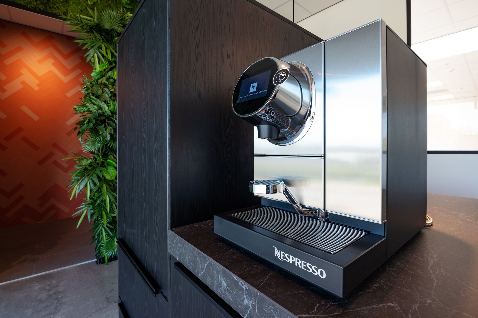 Een moderne zwarte Nespresso-koffiemachine op een aanrecht met een donkerhouten kast.