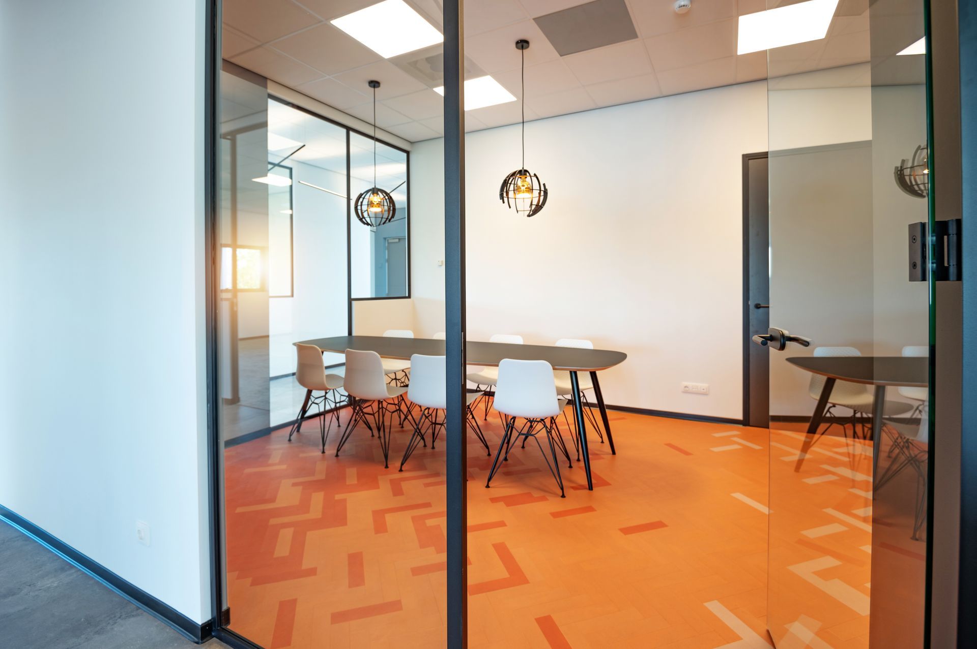 Moderne vergaderruimte met glazen wanden, tafel, stoelen en een oranje vloer met patroon.