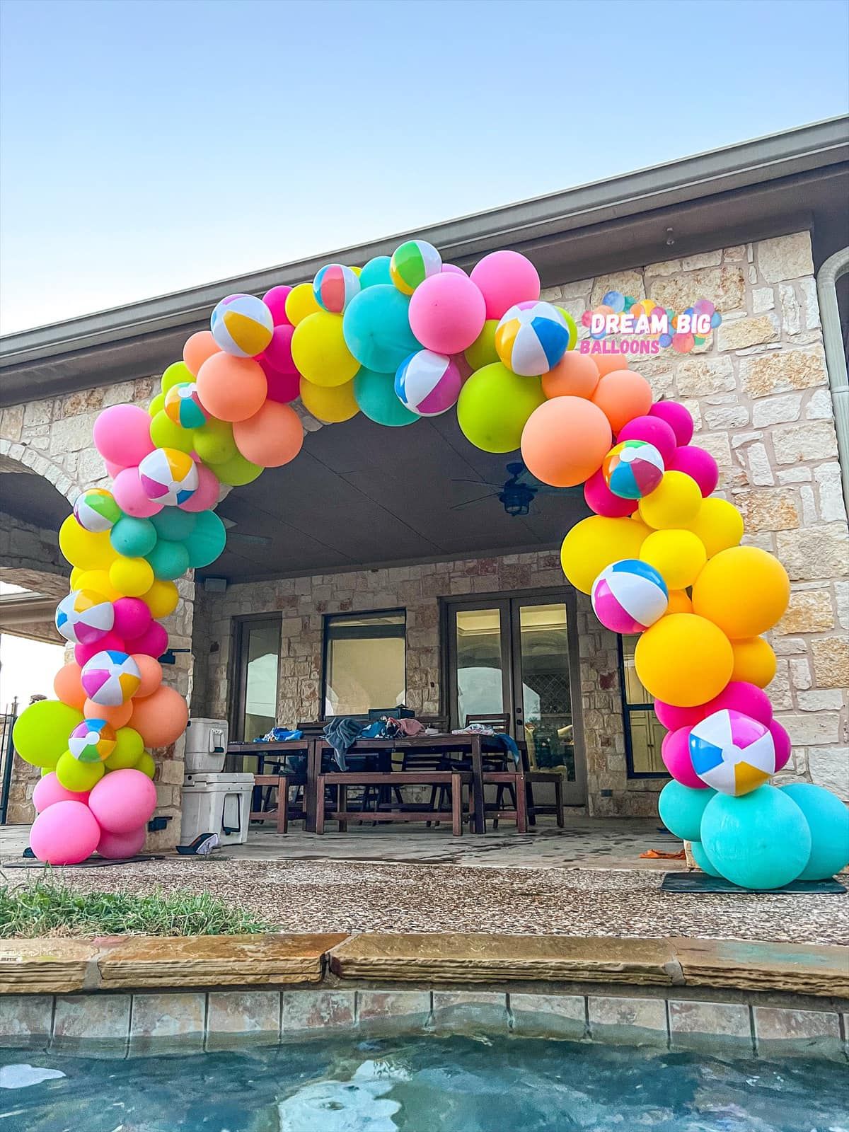a colorful balloon arch is sitting next to a pool in front of a house