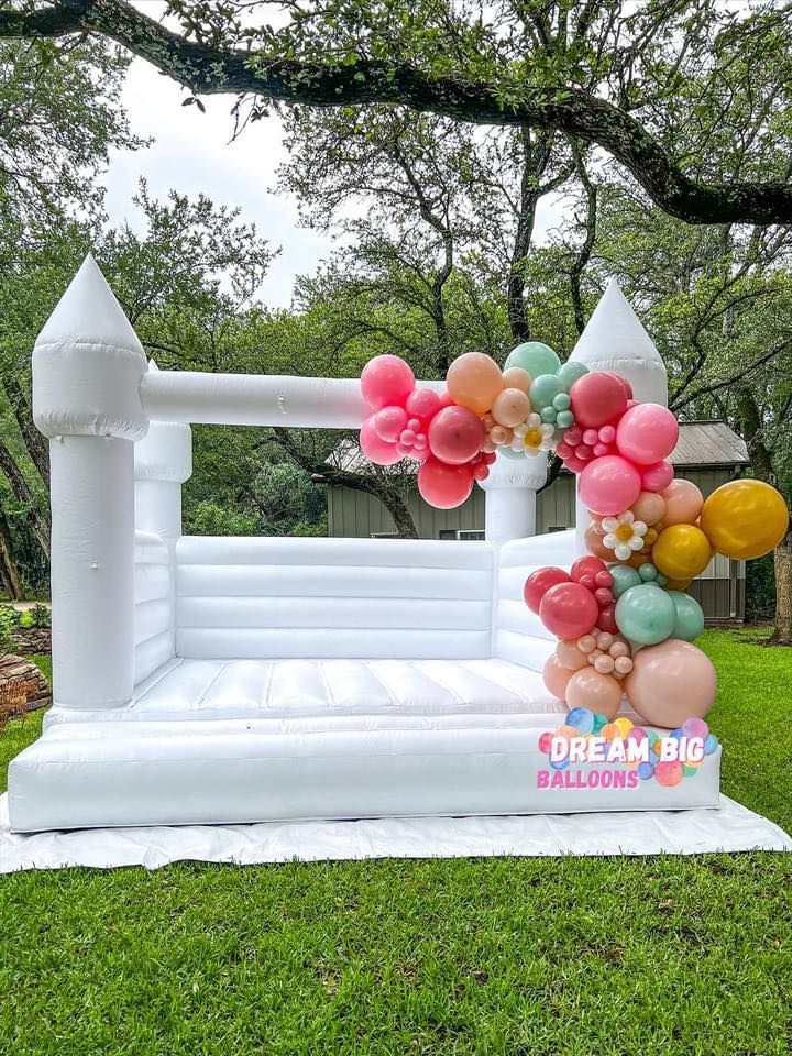 a white bouncy castle decorated with balloons is sitting on top of a lush green field