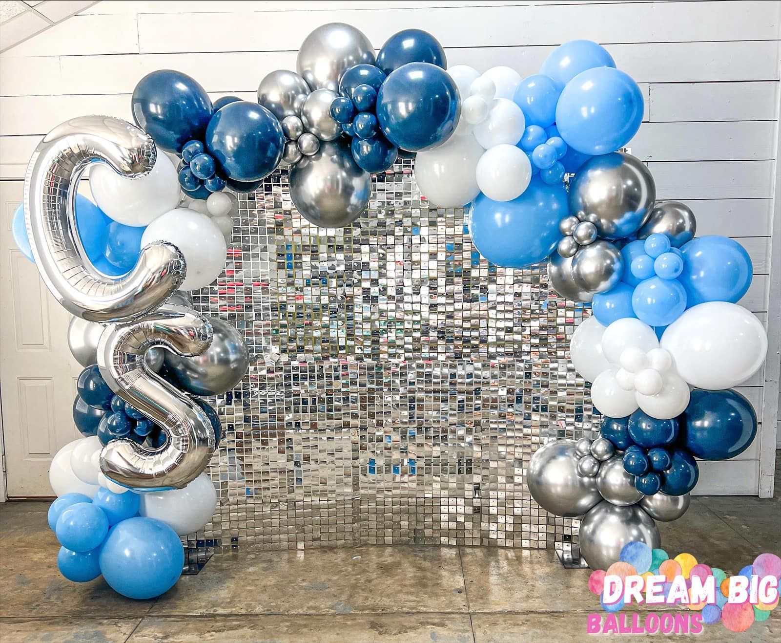 a wall covered in blue , white , and silver balloons