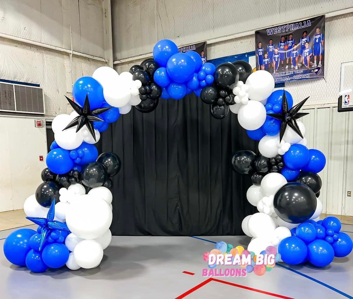 a blue , white and black balloon arch in a gym