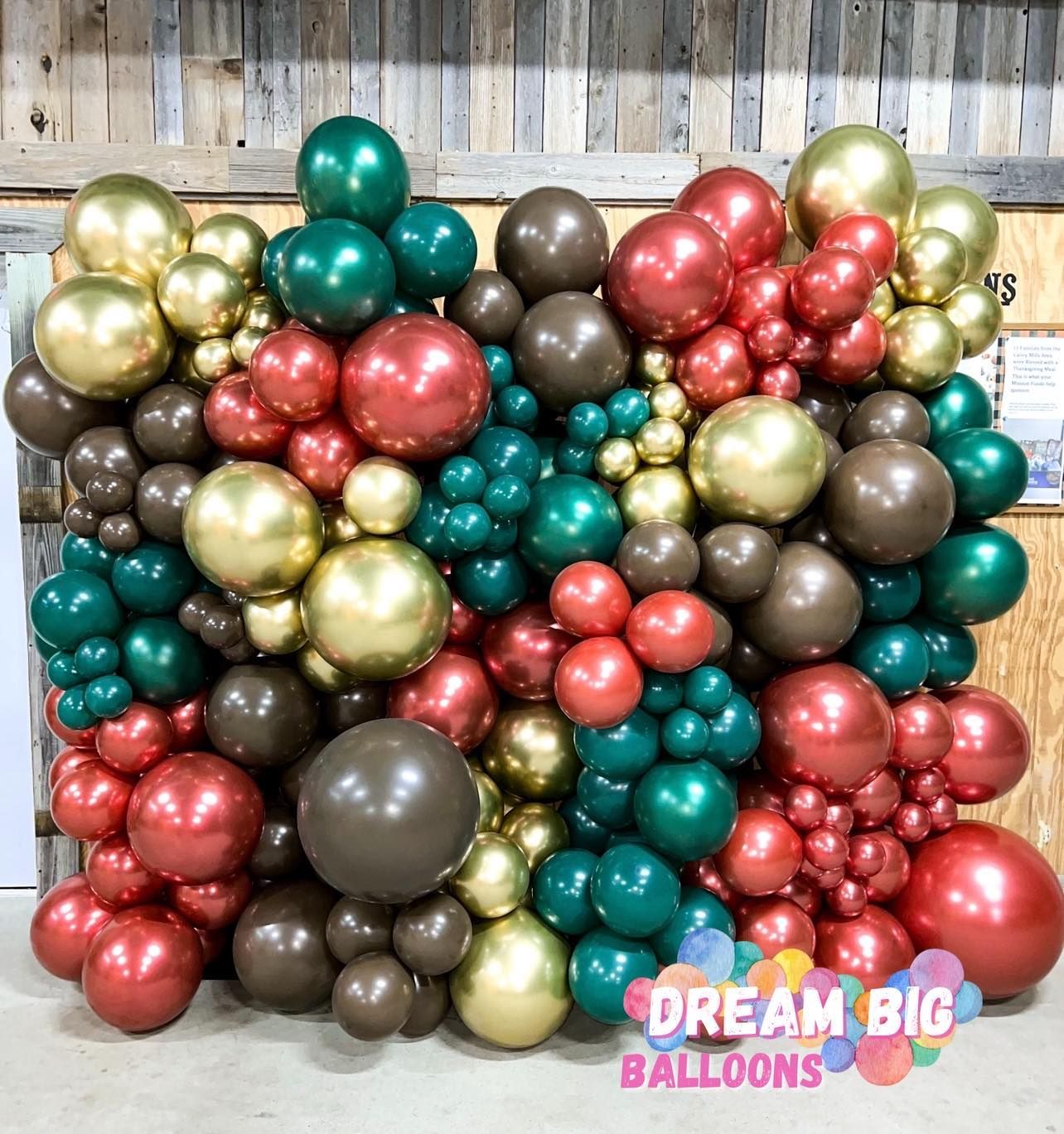 A wall filled with red , green , and gold balloons.