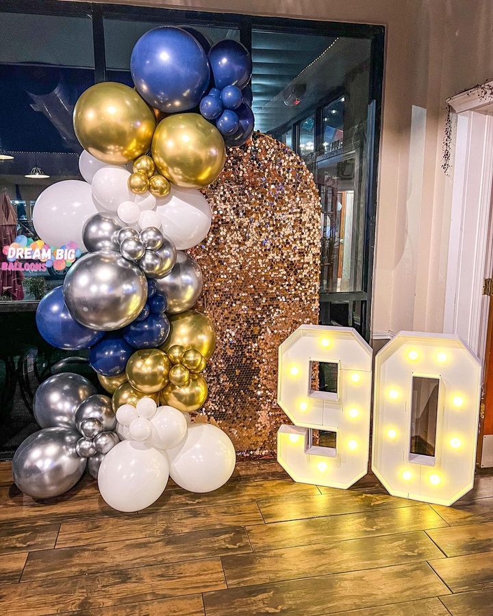 A bunch of balloons are sitting on top of a wooden floor next to a sign that says 90.