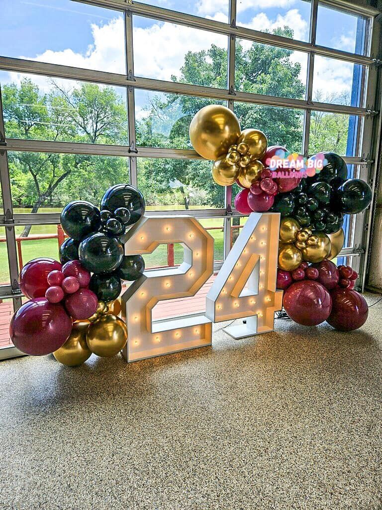 A large number 24 is surrounded by balloons in front of a garage door.