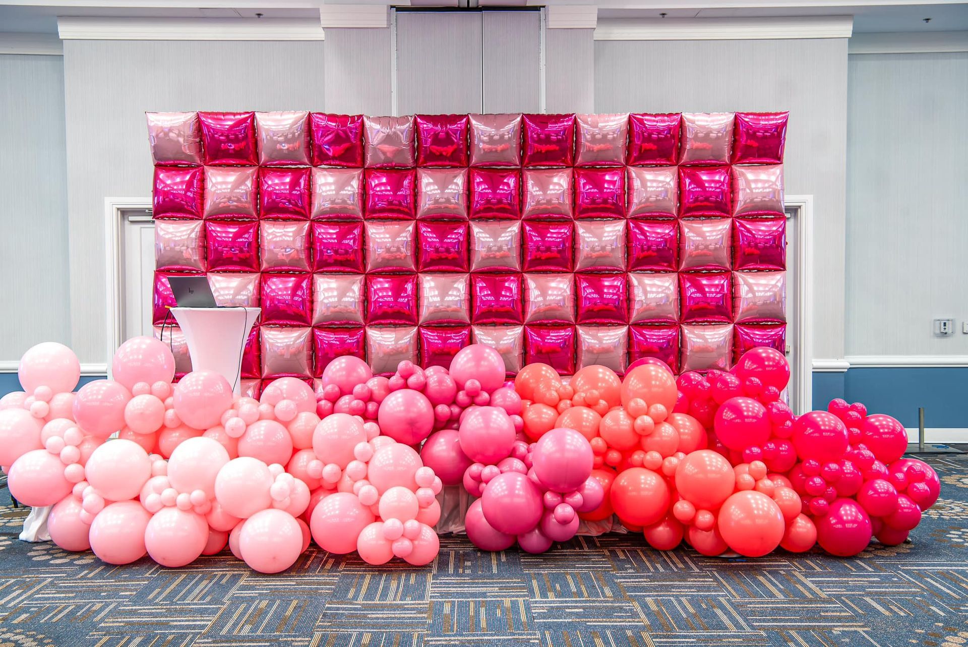 A wall made of pink and red balloons in a room.