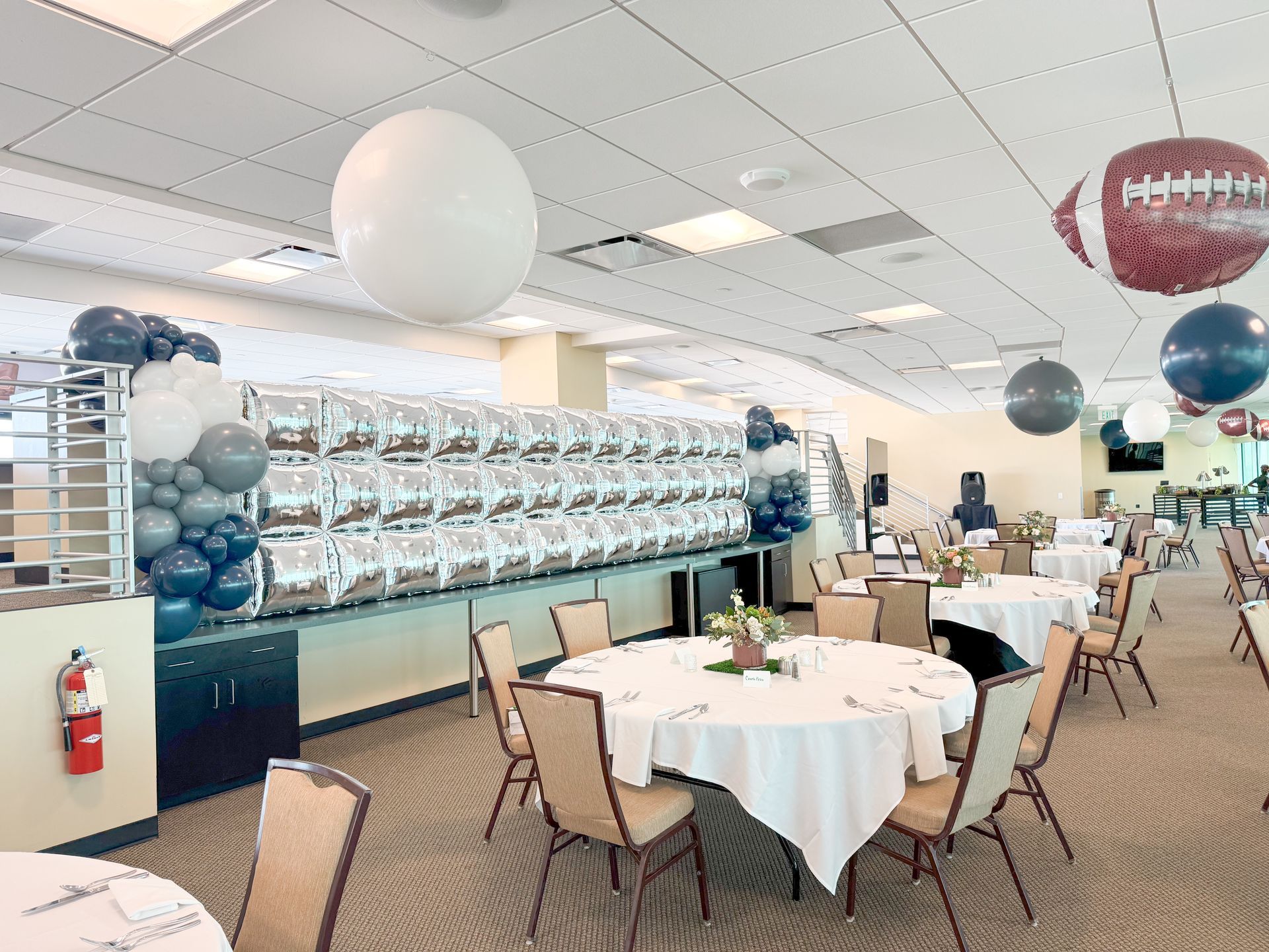 A large room with tables and chairs and balloons hanging from the ceiling.
