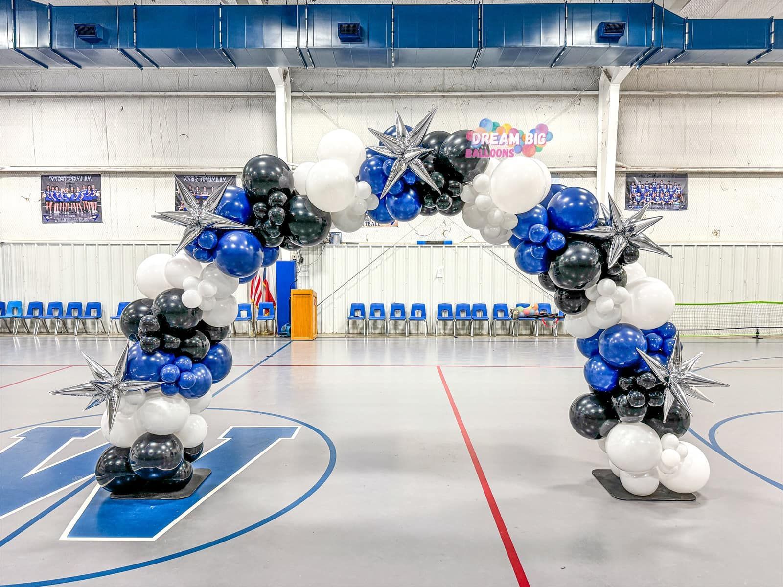 A basketball court decorated with blue , white and black balloons.