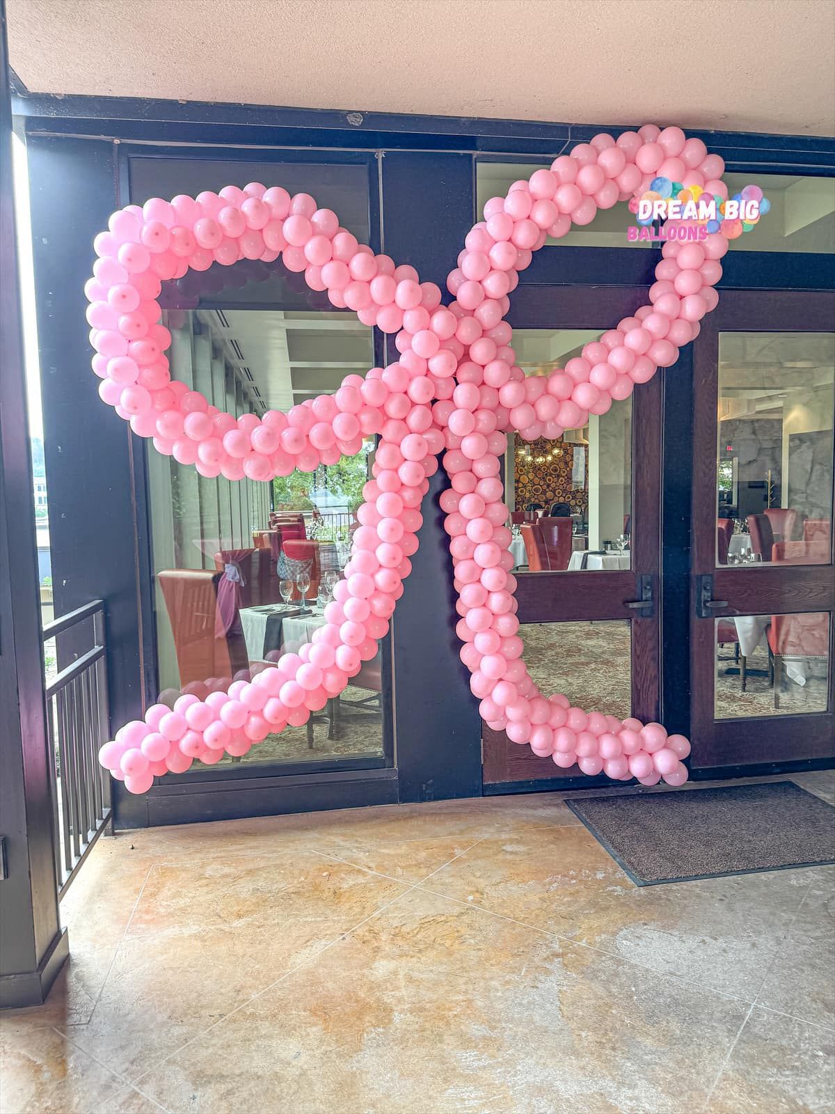 A large pink bow made of balloons is hanging on a door.
