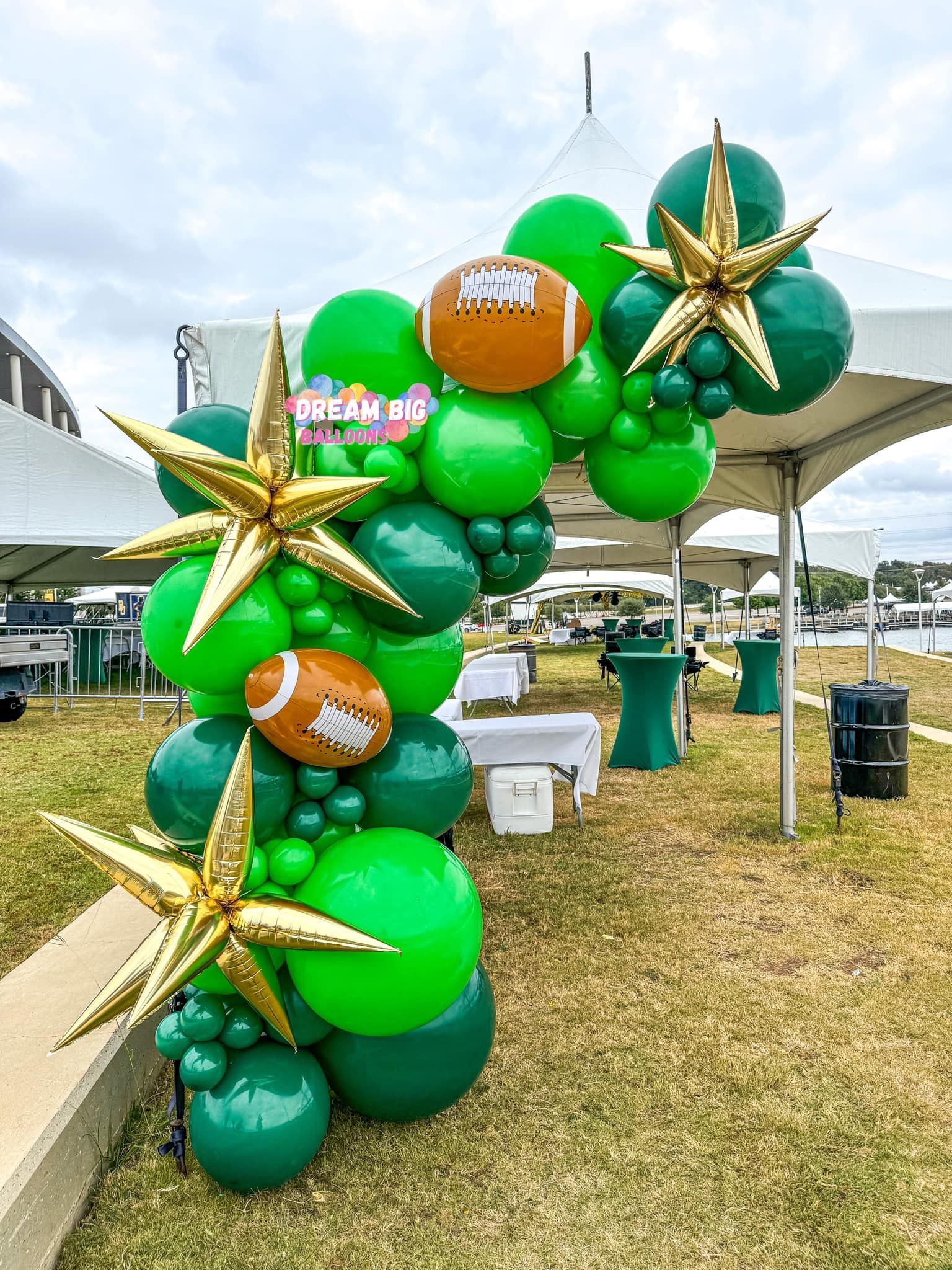 A bunch of green and gold balloons are sitting on top of each other in a field.