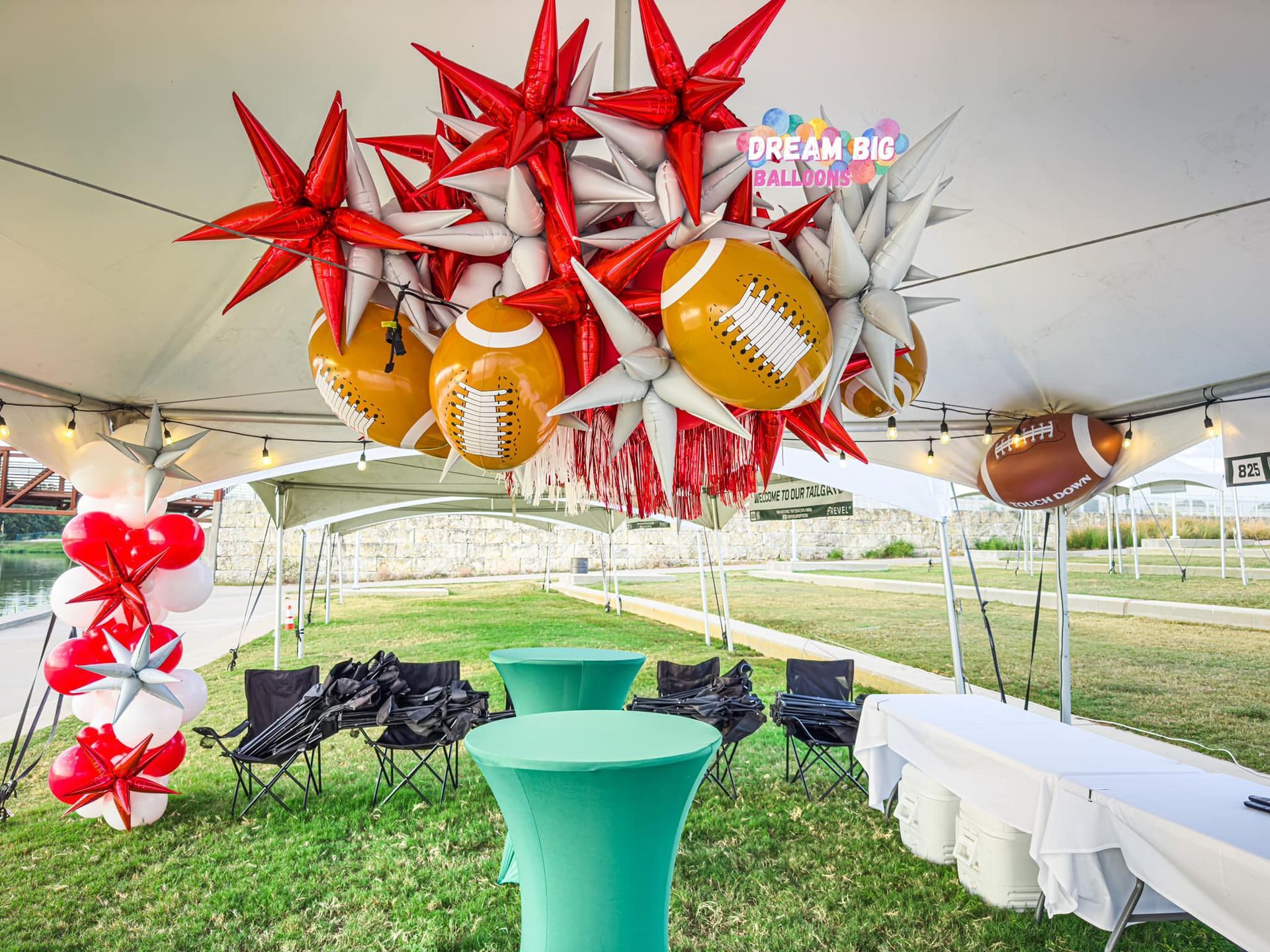 A tent with tables and chairs underneath it and balloons hanging from the ceiling.