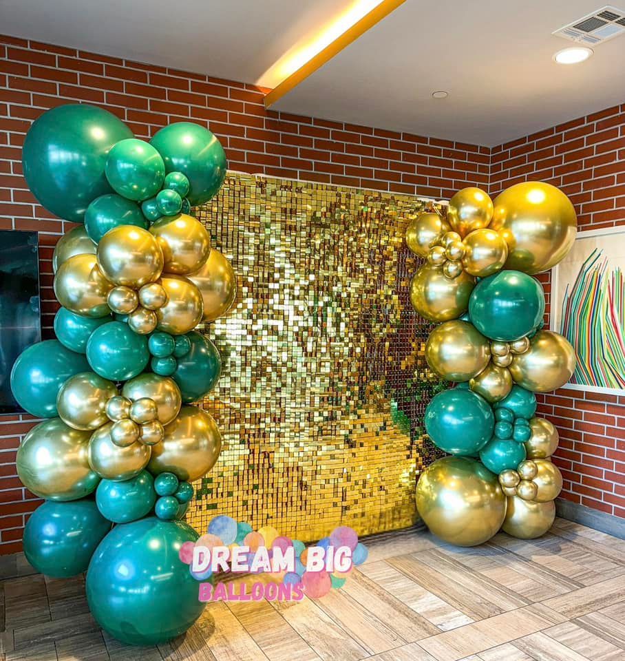 A room filled with green and gold balloons and a brick wall.