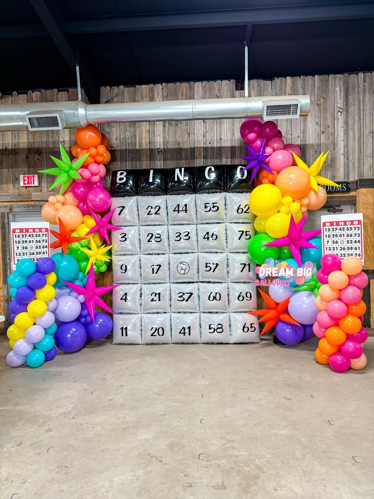 A bunch of colorful balloons are sitting in front of a bingo board.