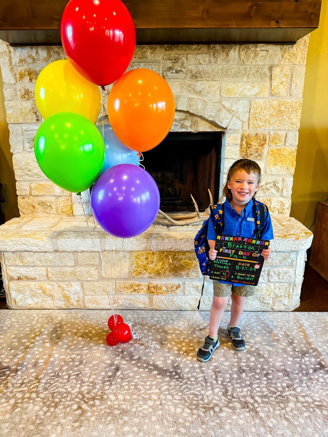 A young boy is standing in front of a fireplace with balloons.