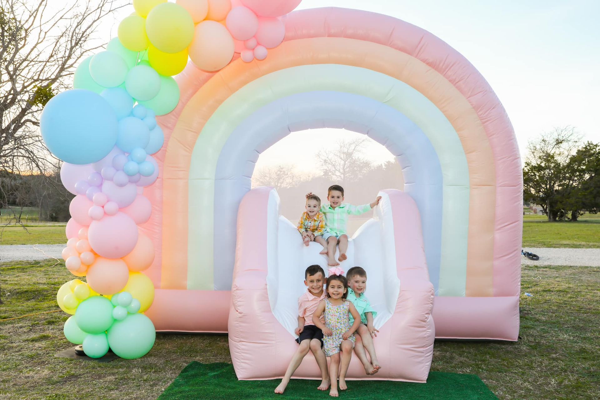 A group of children are sitting on top of an inflatable rainbow slide.