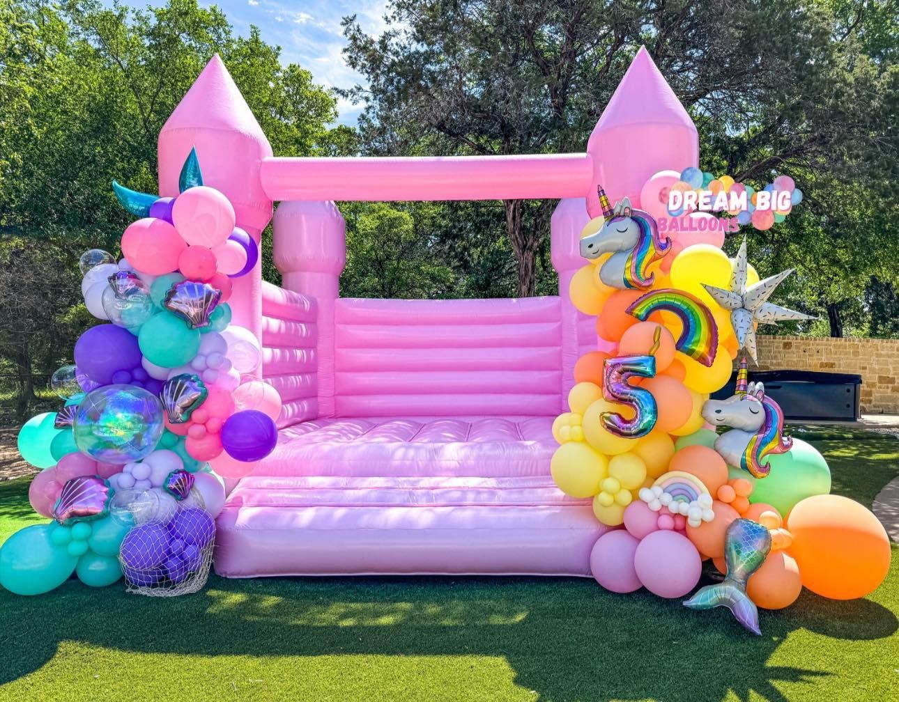 A pink bouncy house is decorated with balloons for a birthday party.