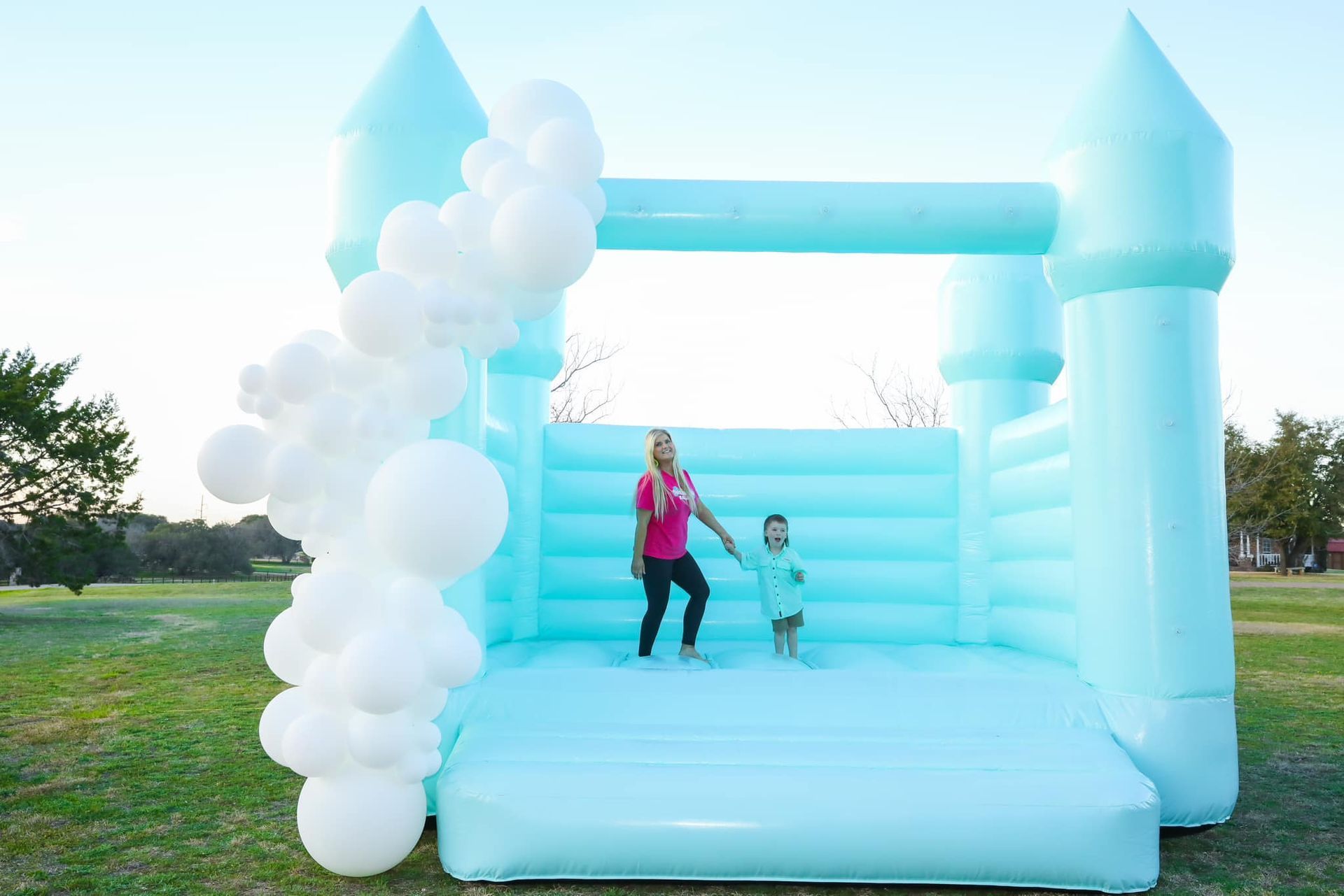 A woman and a child are standing in front of a blue bouncy castle.
