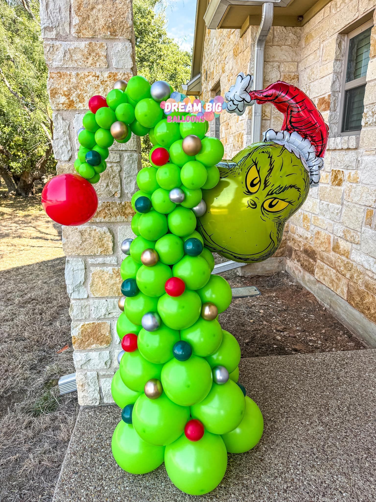 A christmas tree made of balloons is sitting on the sidewalk in front of a building.