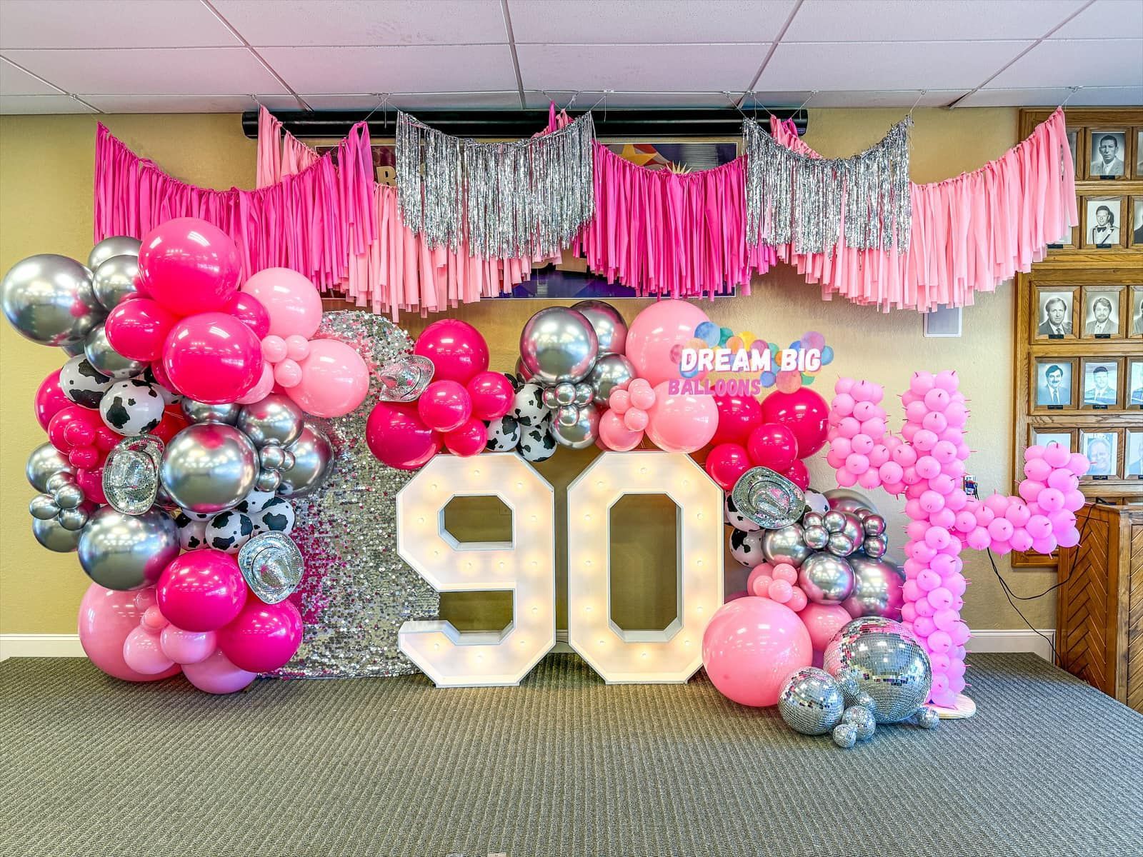 A room decorated with pink , silver and white balloons for a 90th birthday party.