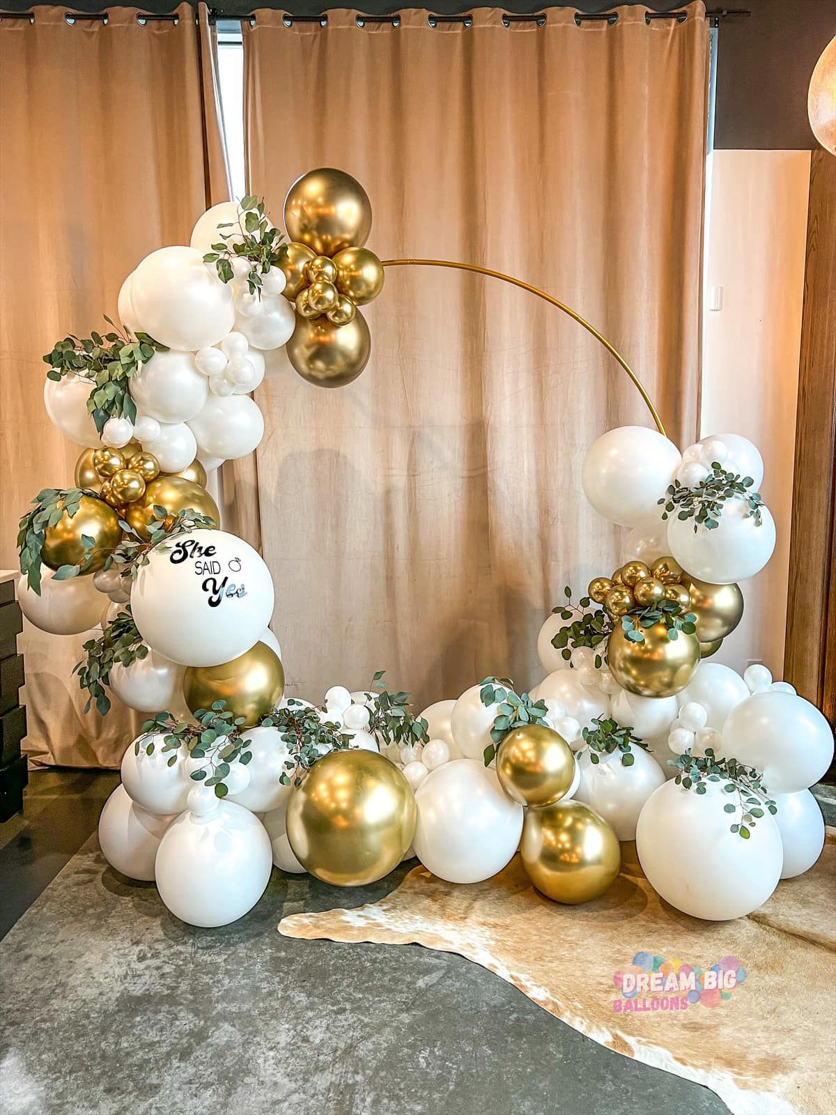 a room filled with white and gold balloons and greenery
