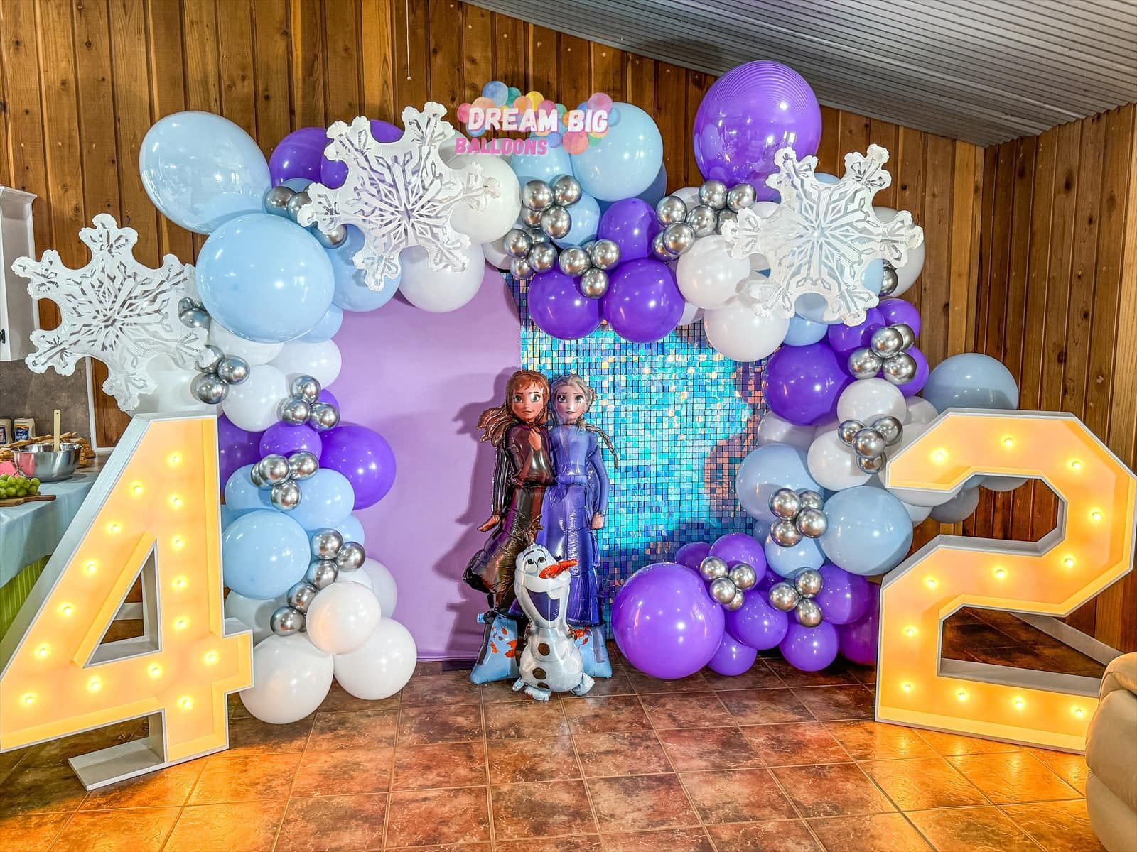 A girl is standing in front of a wall decorated with balloons and snowflakes.