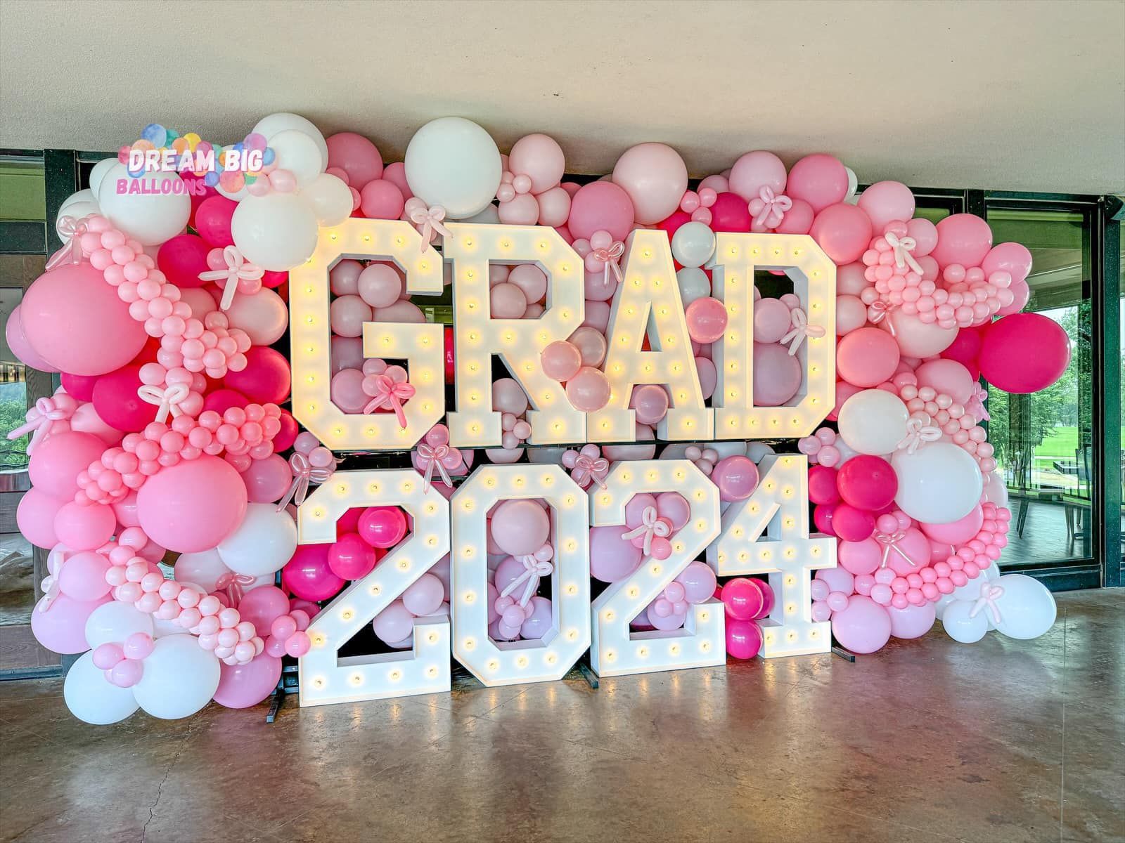 A wall filled with pink and white balloons and the words `` grad 2024 ''.