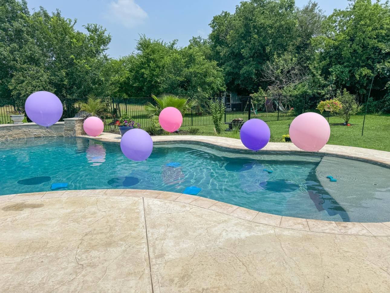 Pink and purple balloons are floating in a swimming pool