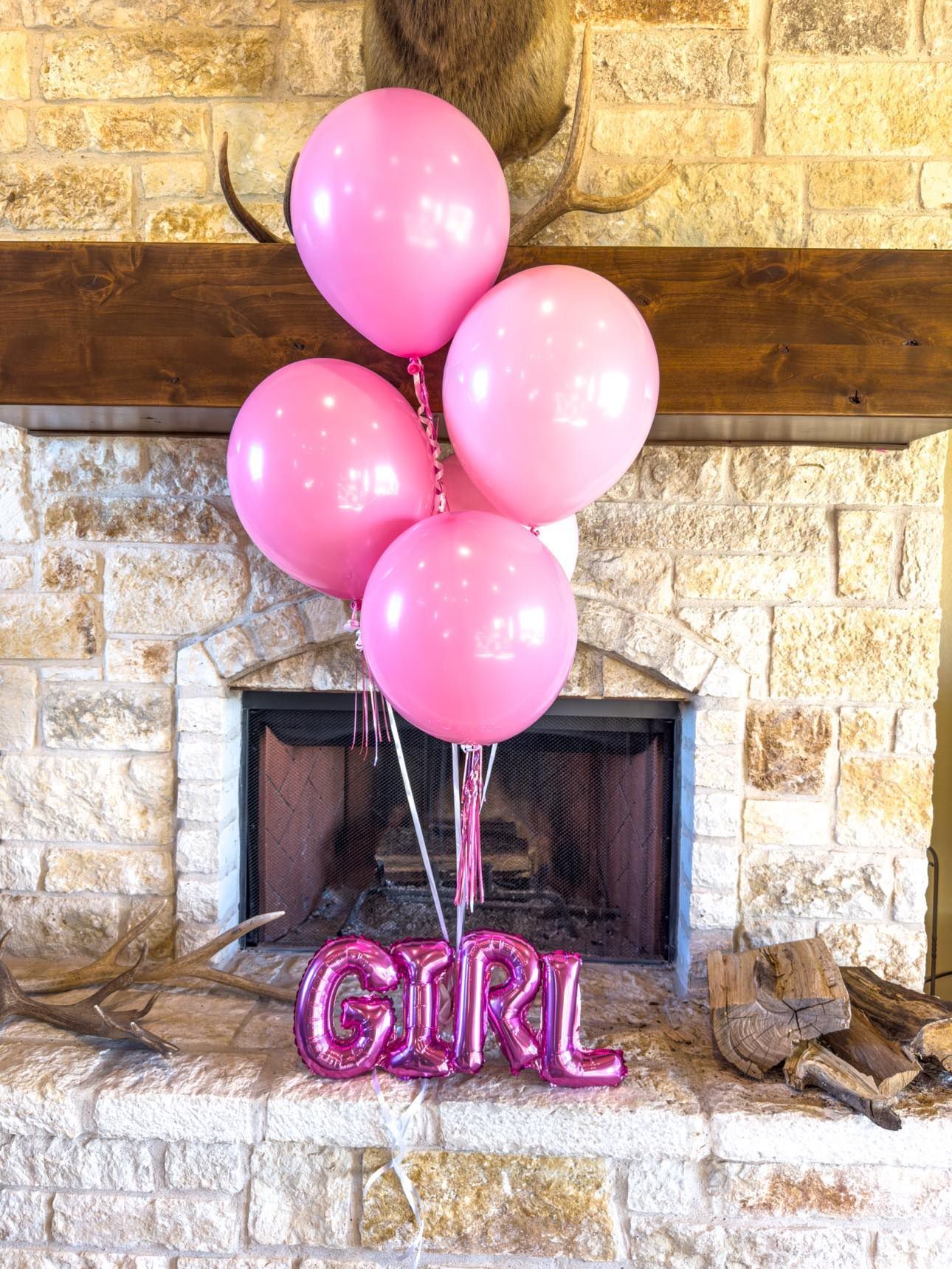 A bunch of pink balloons sitting in front of a fireplace that say