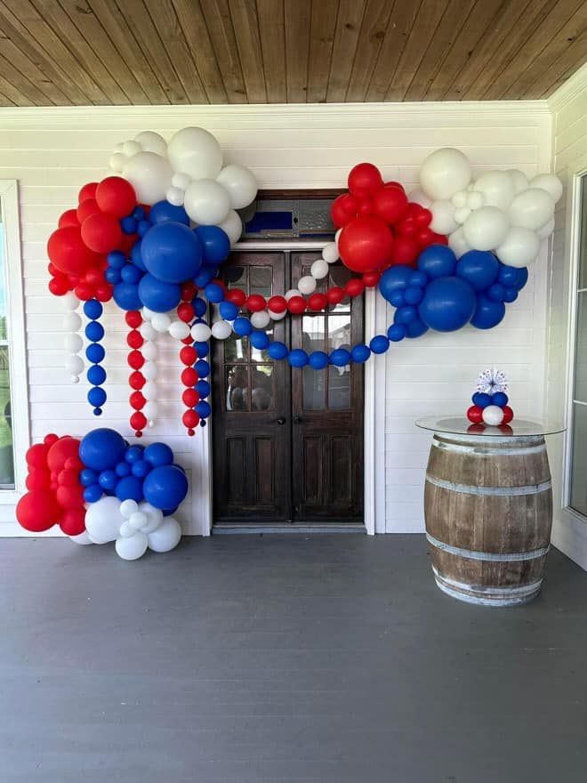 A porch decorated with red , white and blue balloons and a wooden barrel.