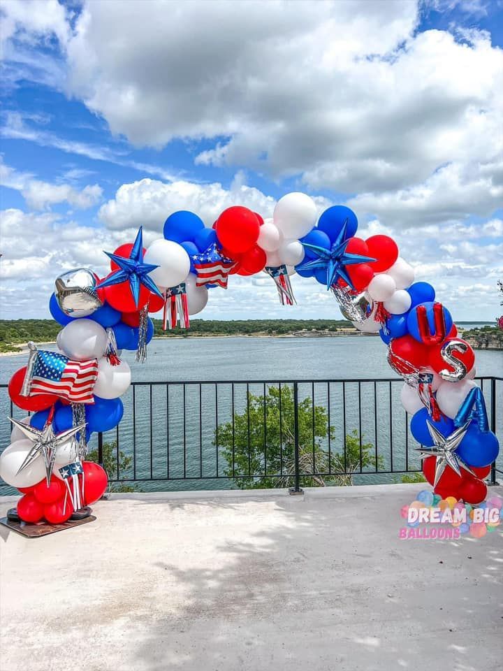 A red , white and blue balloon arch overlooking a lake.