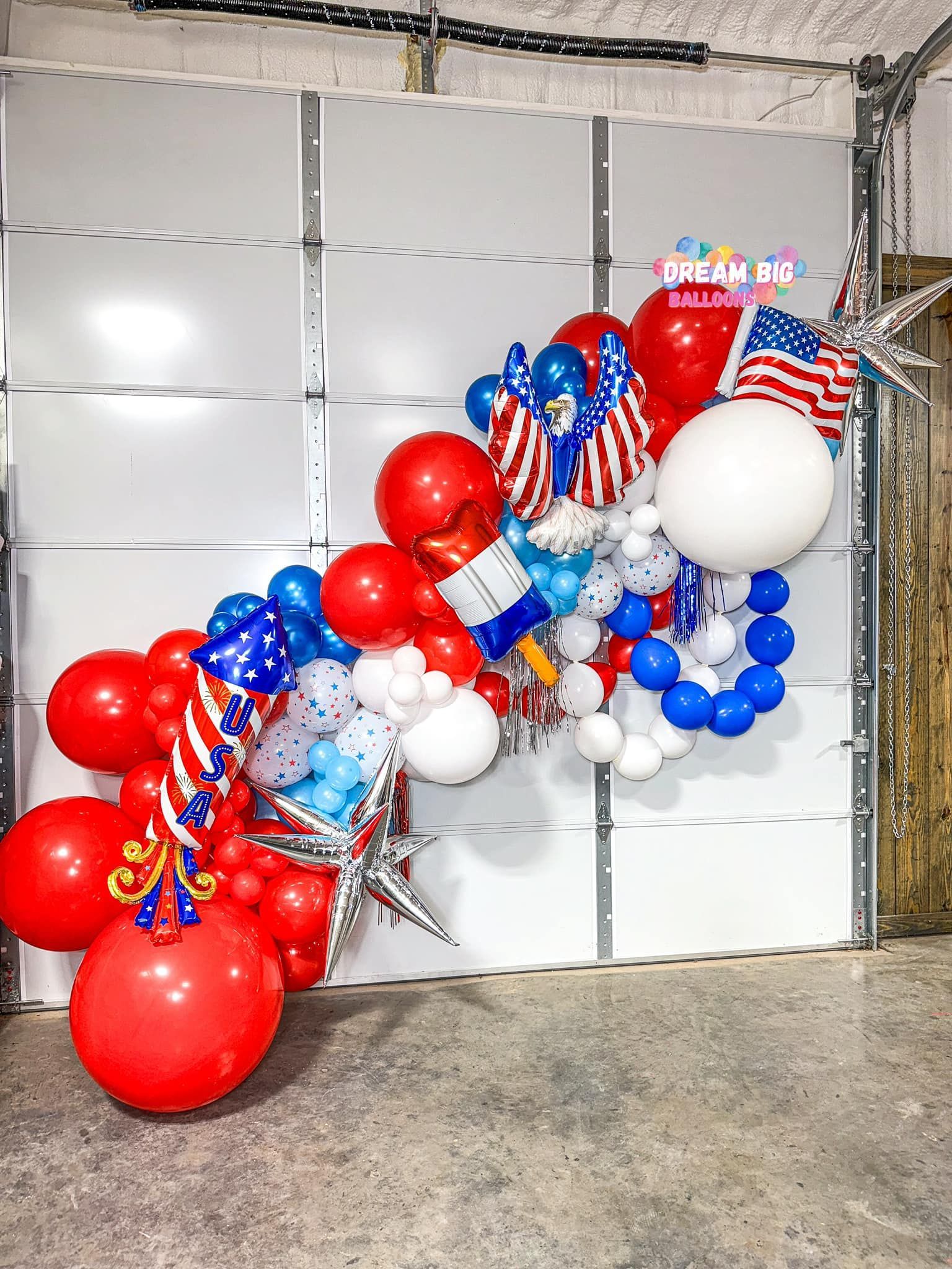 A bunch of red , white , and blue balloons are sitting on a garage door.