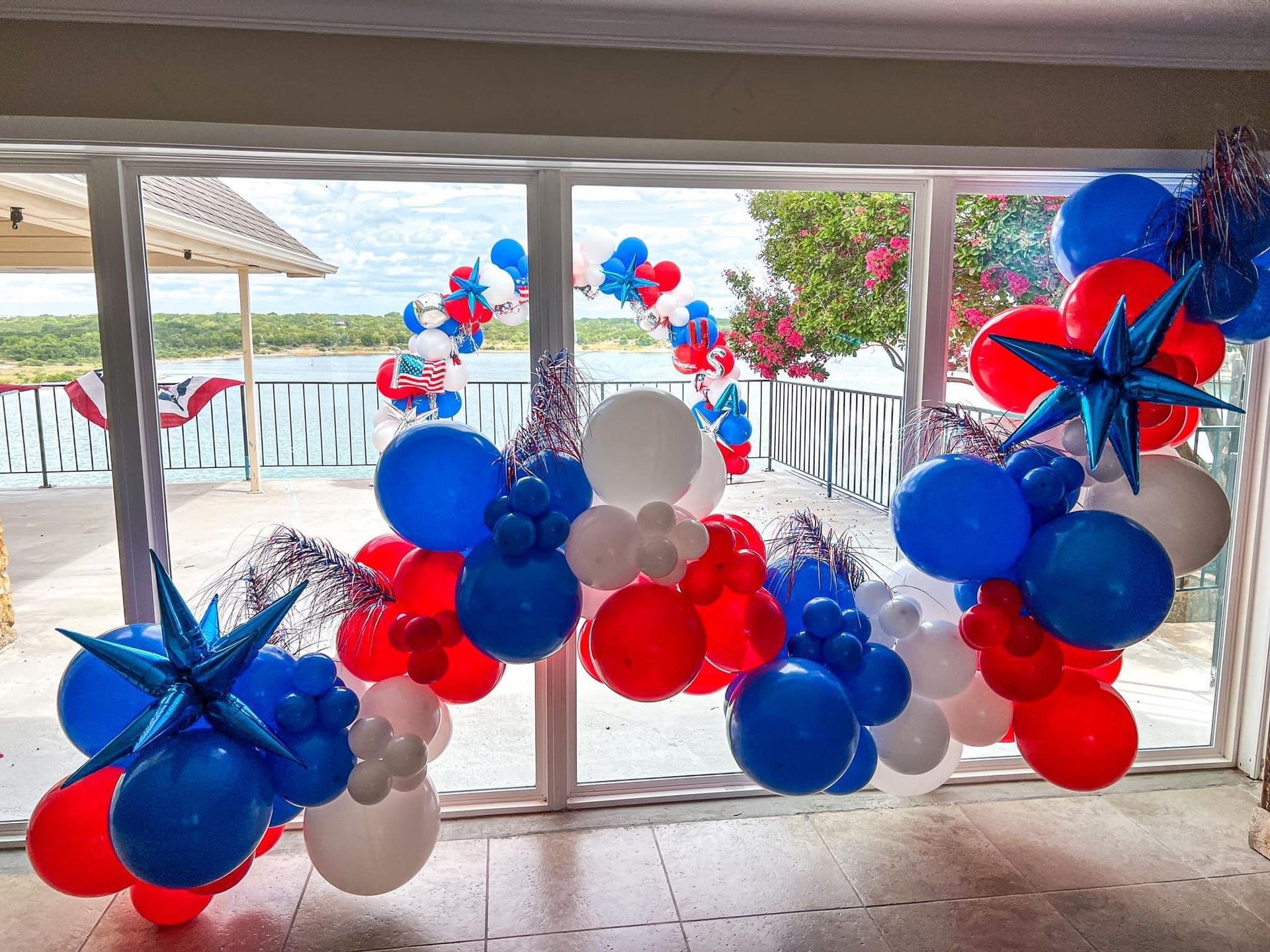 A bunch of red , white and blue balloons are hanging from a window.