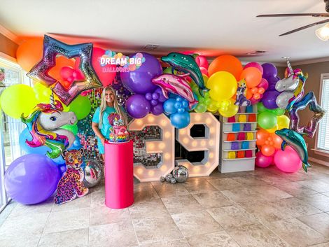 A woman is standing in front of a wall filled with colorful balloons.