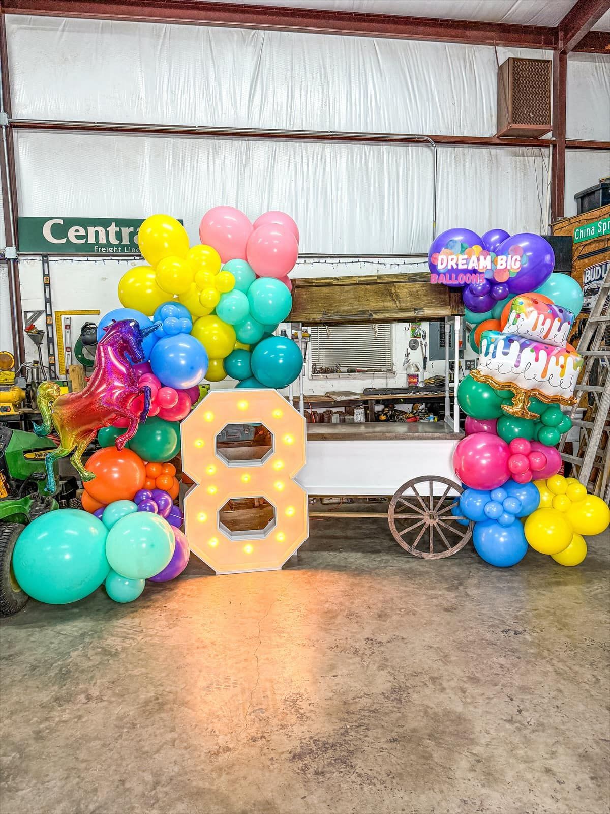A large number eight is surrounded by balloons in a garage.