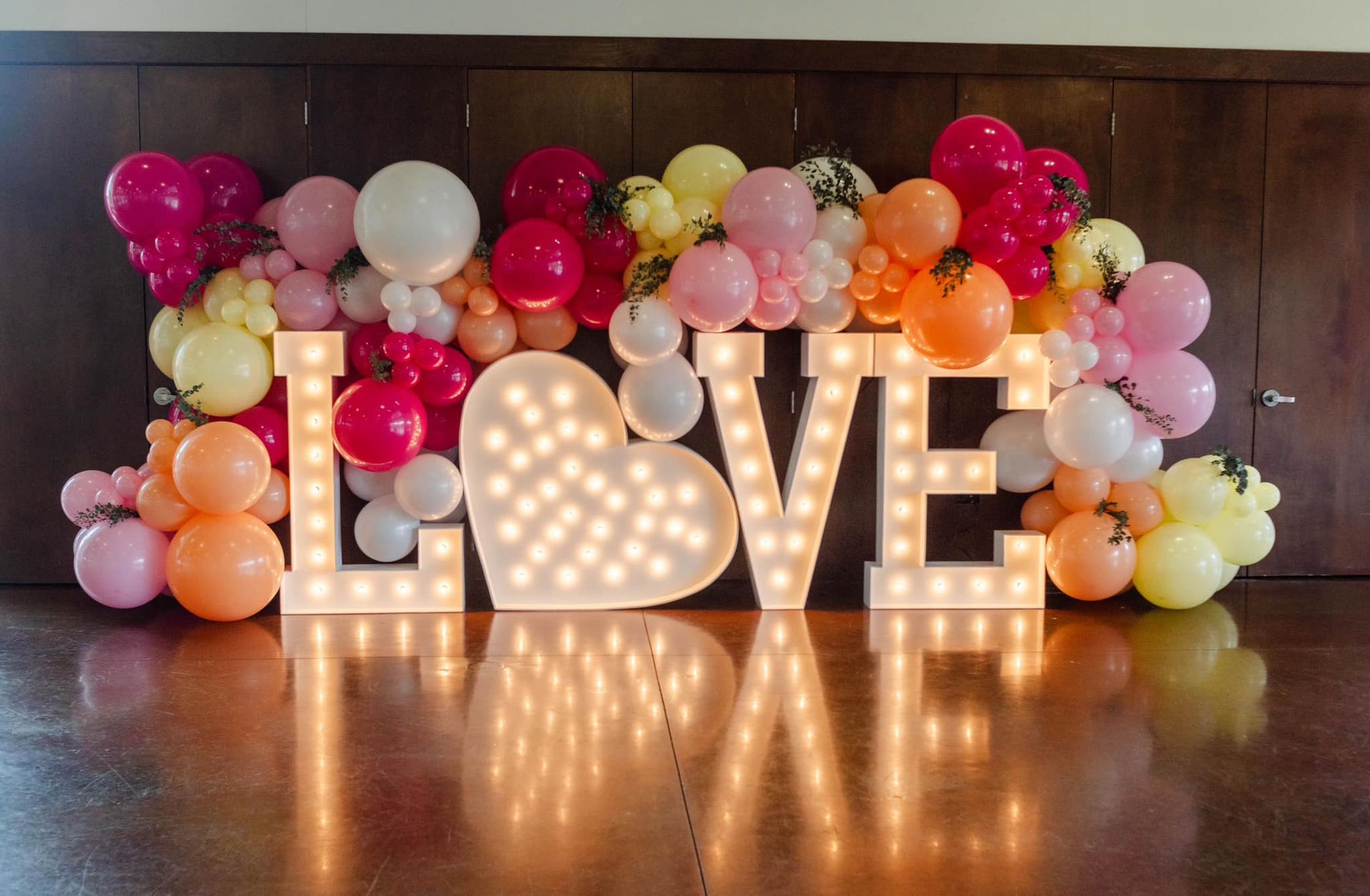 The word love is surrounded by balloons and lights.