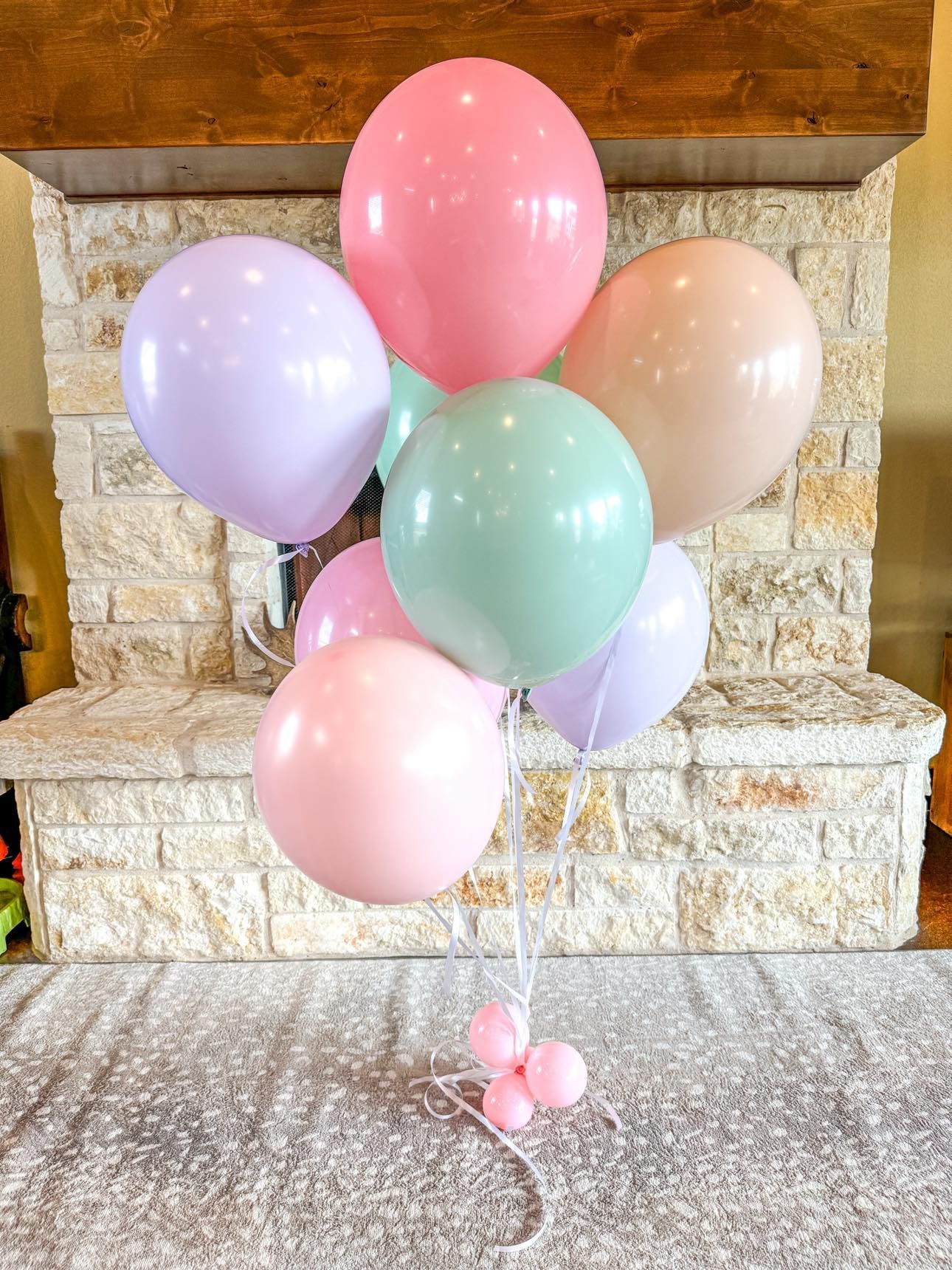 A bunch of pastel helium balloons are sitting in front of a fireplace.