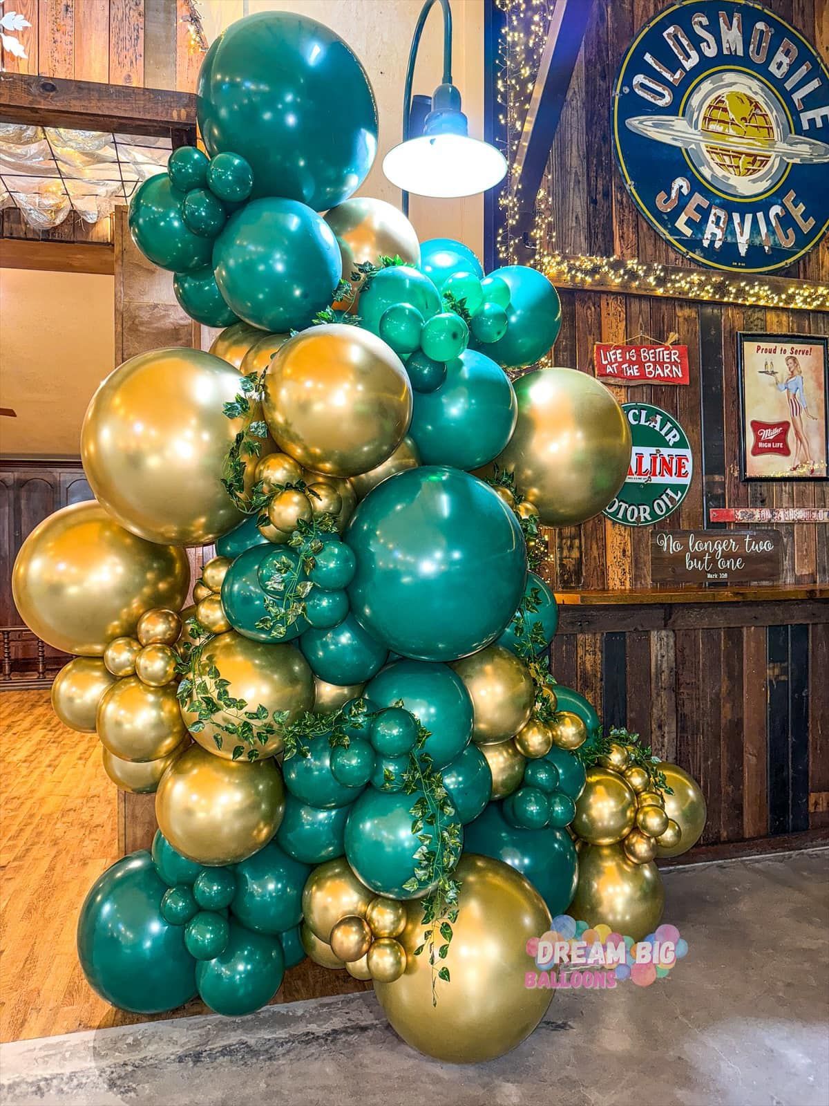 A bunch of green and gold balloons are stacked on top of each other in a room.